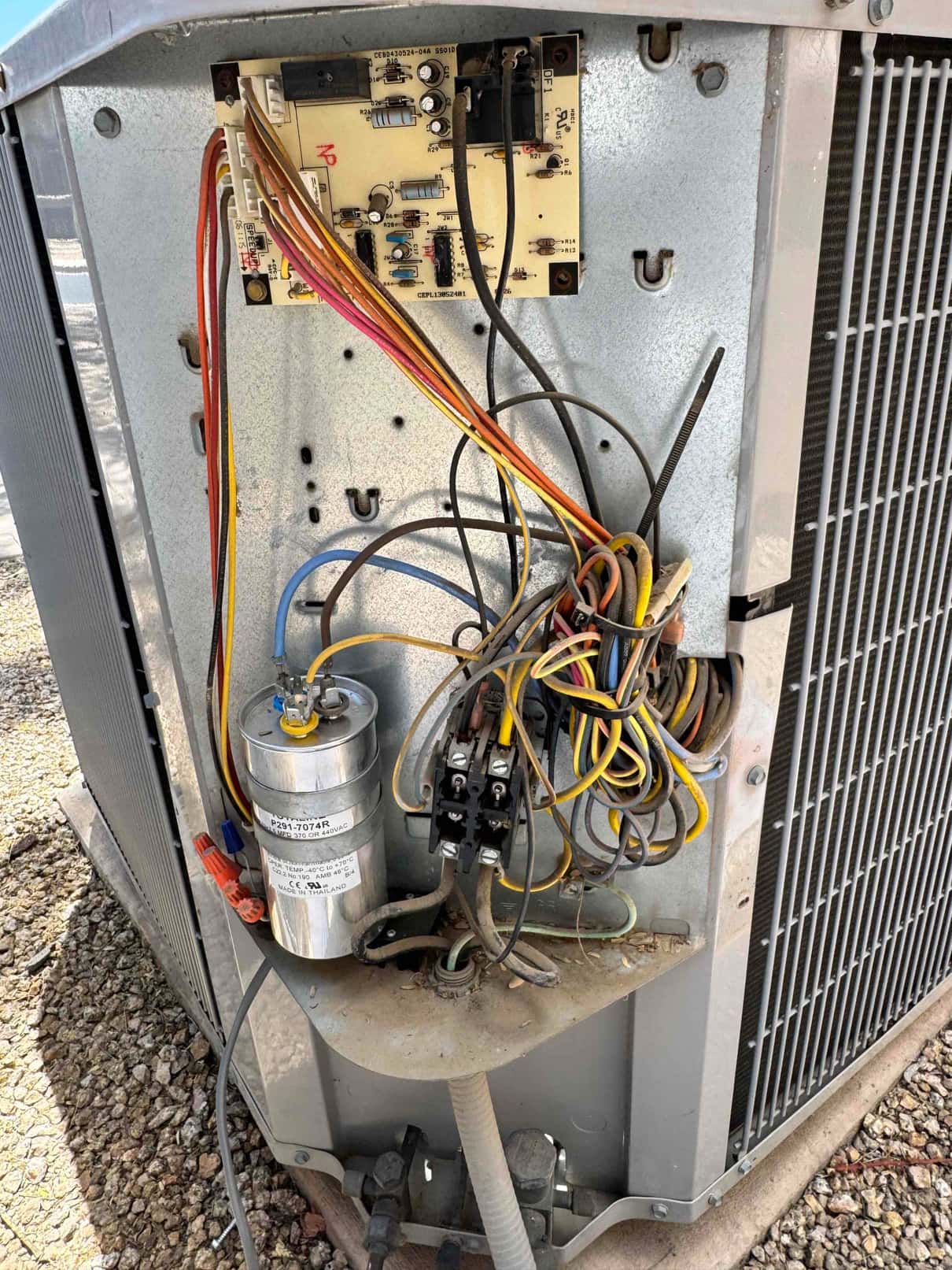 Outdoor condenser panel open showing control board, contactor, dual-run capacitor, and connected wiring inside the unit.