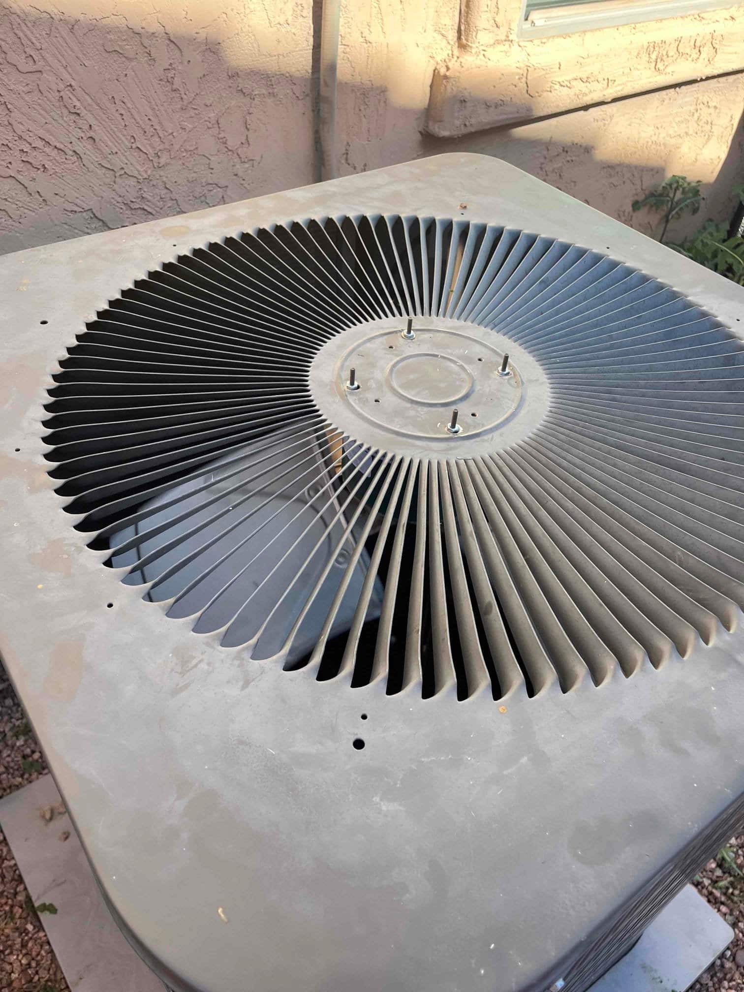 Outdoor condenser top panel showing circular fan guard with exposed mounting studs, with no fan motor visible.