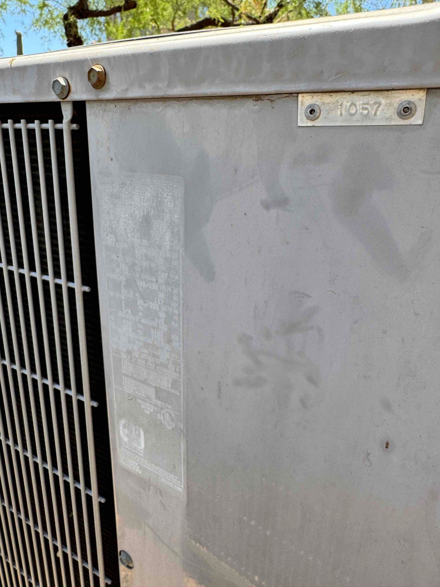 Outdoor condenser unit side panel showing coil grille, faded equipment label, and light surface oxidation on the cabinet.