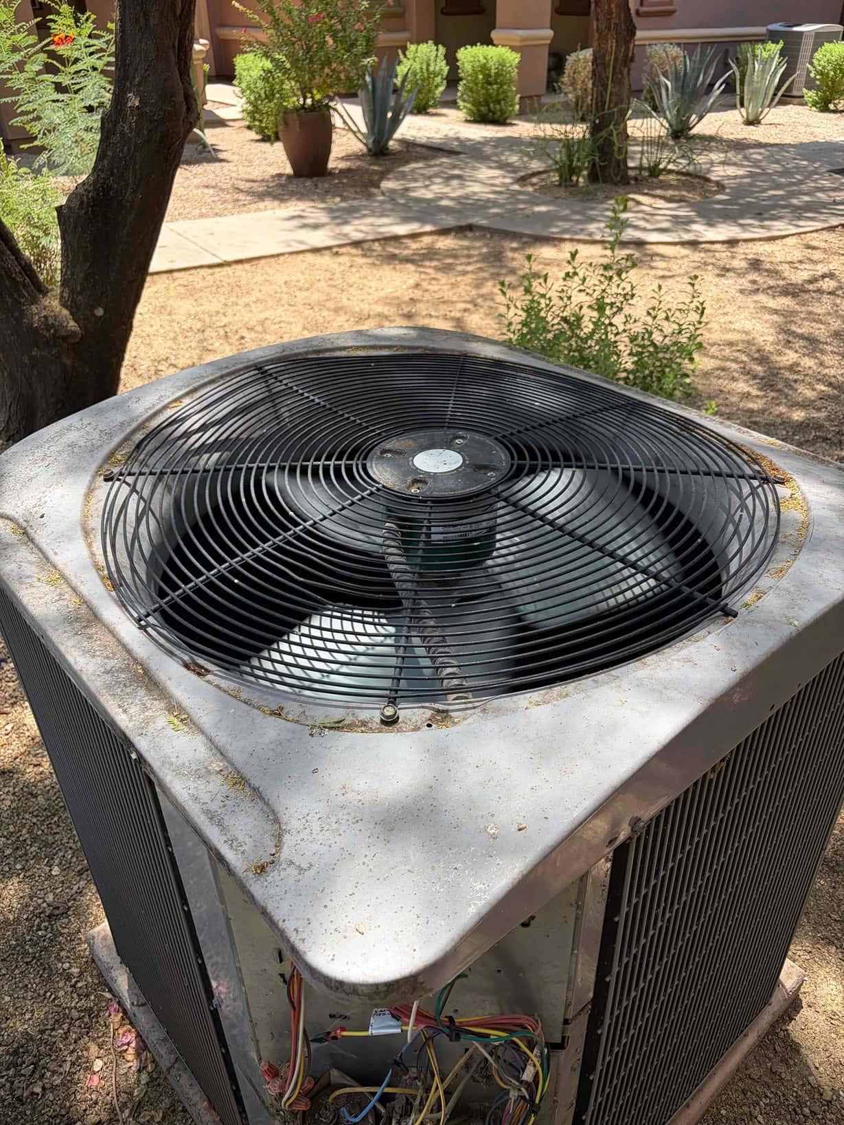 Outdoor condenser unit with top fan grille, dust and debris on cabinet, and electrical compartment open showing wiring.