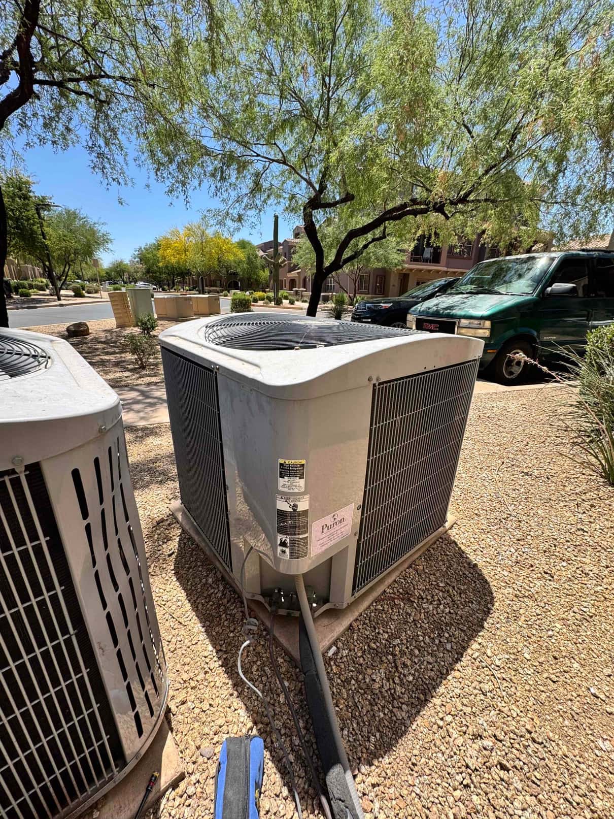 Two outdoor condenser units on gravel pads, with insulated refrigerant lines and service valves visible at the base.
