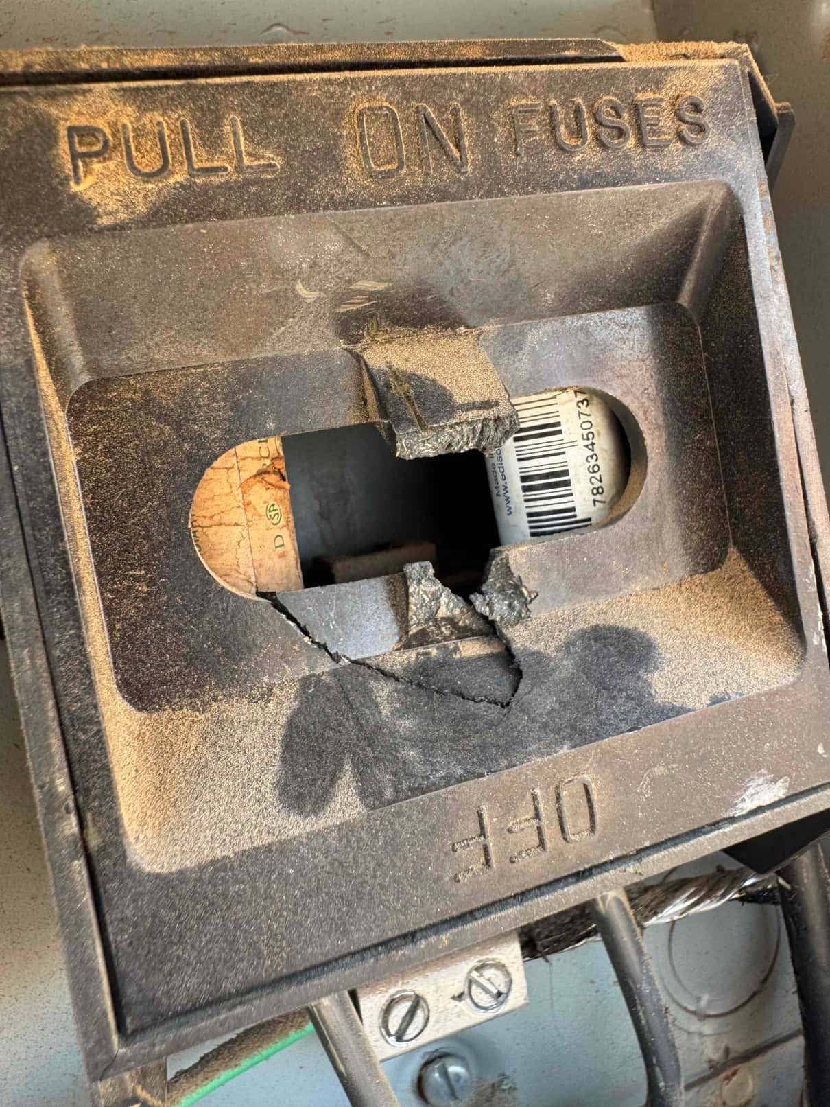 Outdoor disconnect pull-out handle is cracked and missing pieces, exposing a cartridge fuse and internal wiring.