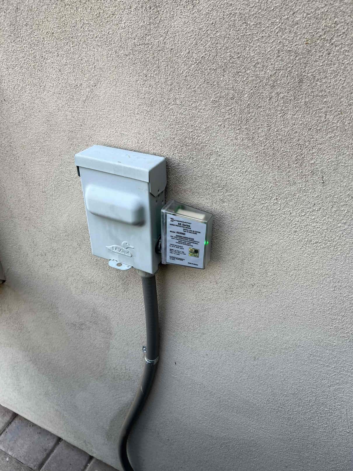 Outdoor HVAC disconnect with conduit and a mounted surge protection device showing a green status indicator light.