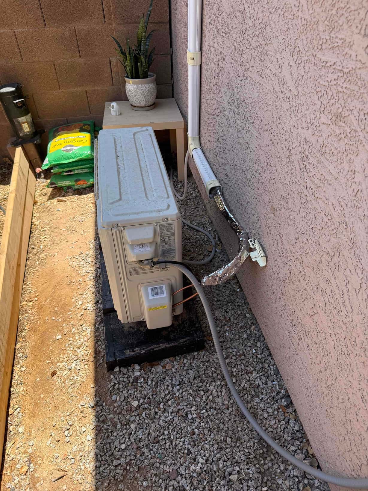 Outdoor mini-split condenser on a pad with line-set cover and insulated refrigerant lines entering the wall.