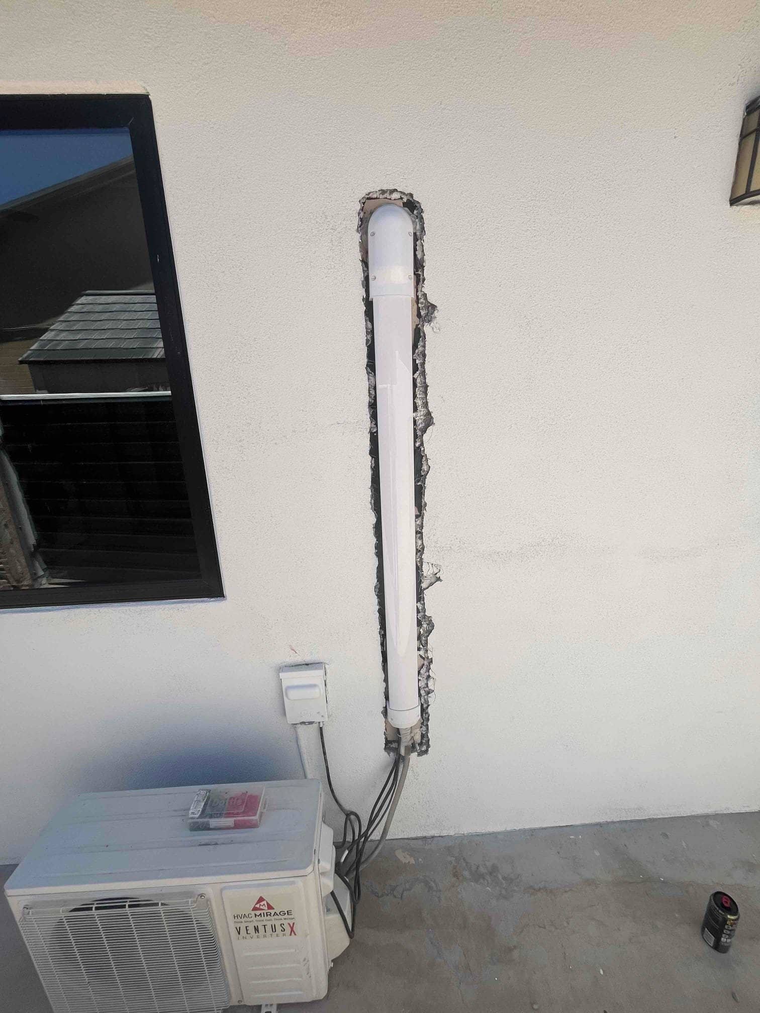 Outdoor mini-split condenser with refrigerant lines and wiring routed through a vertical line-set cover into the stucco wall.