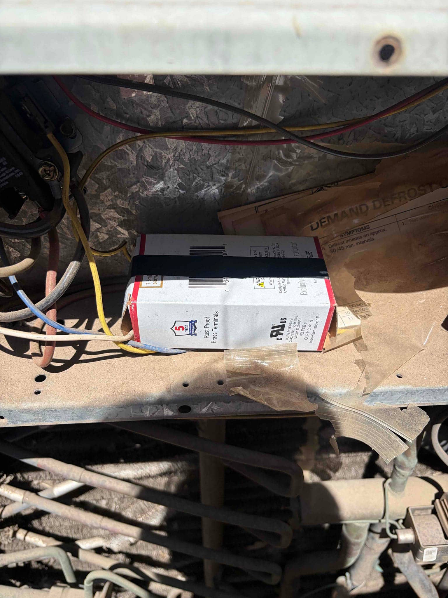 Outdoor unit control compartment shows wiring, dusty metal surface, and capacitor packaging placed inside.