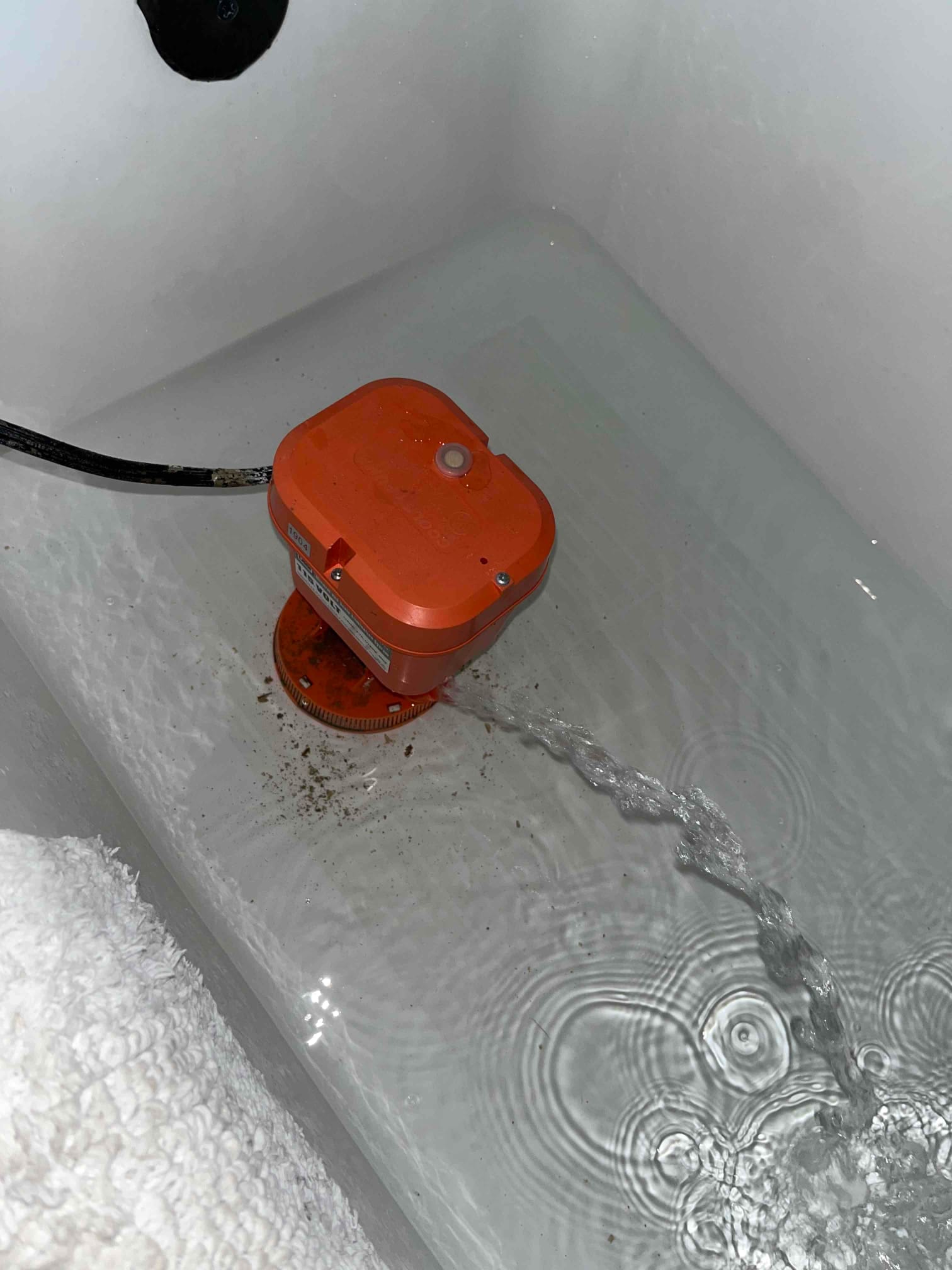 Portable utility pump sits in standing water, discharging a stream through a hose into the bathtub.