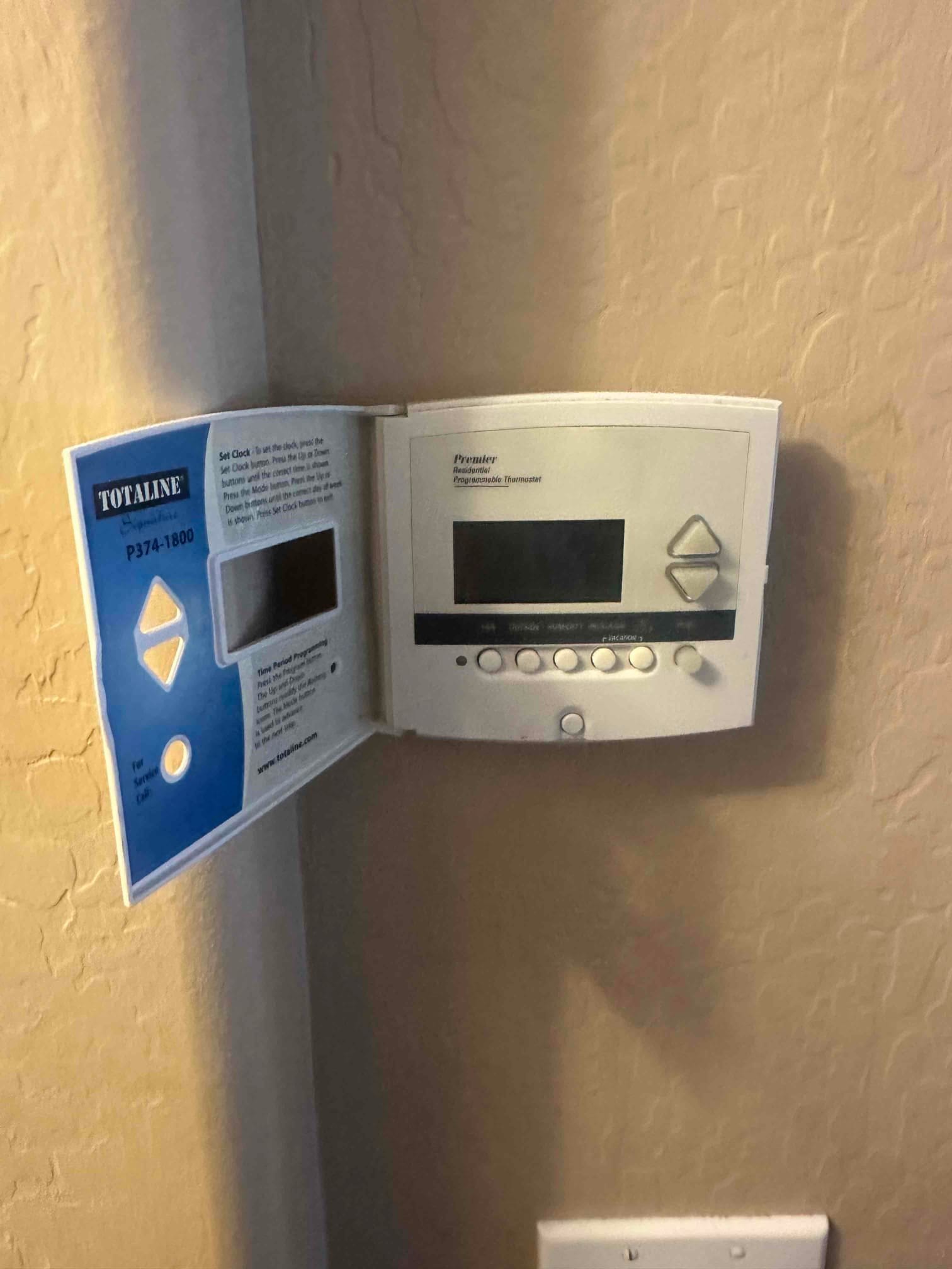 Programmable wall thermostat with the door open, showing digital display, arrow buttons, and multiple control keys.