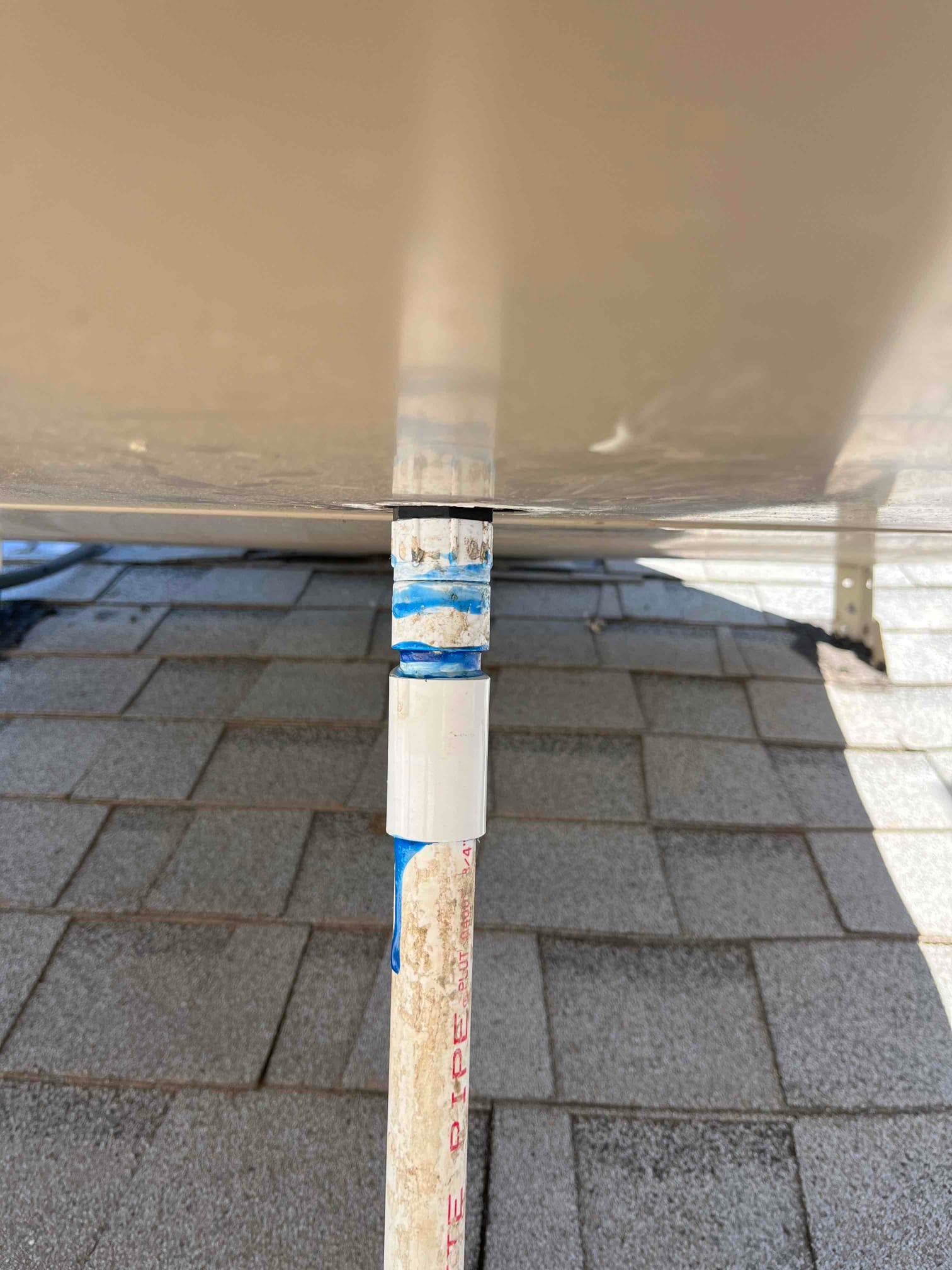 PVC condensate drain line with coupling and blue solvent cement at rooftop unit connection.