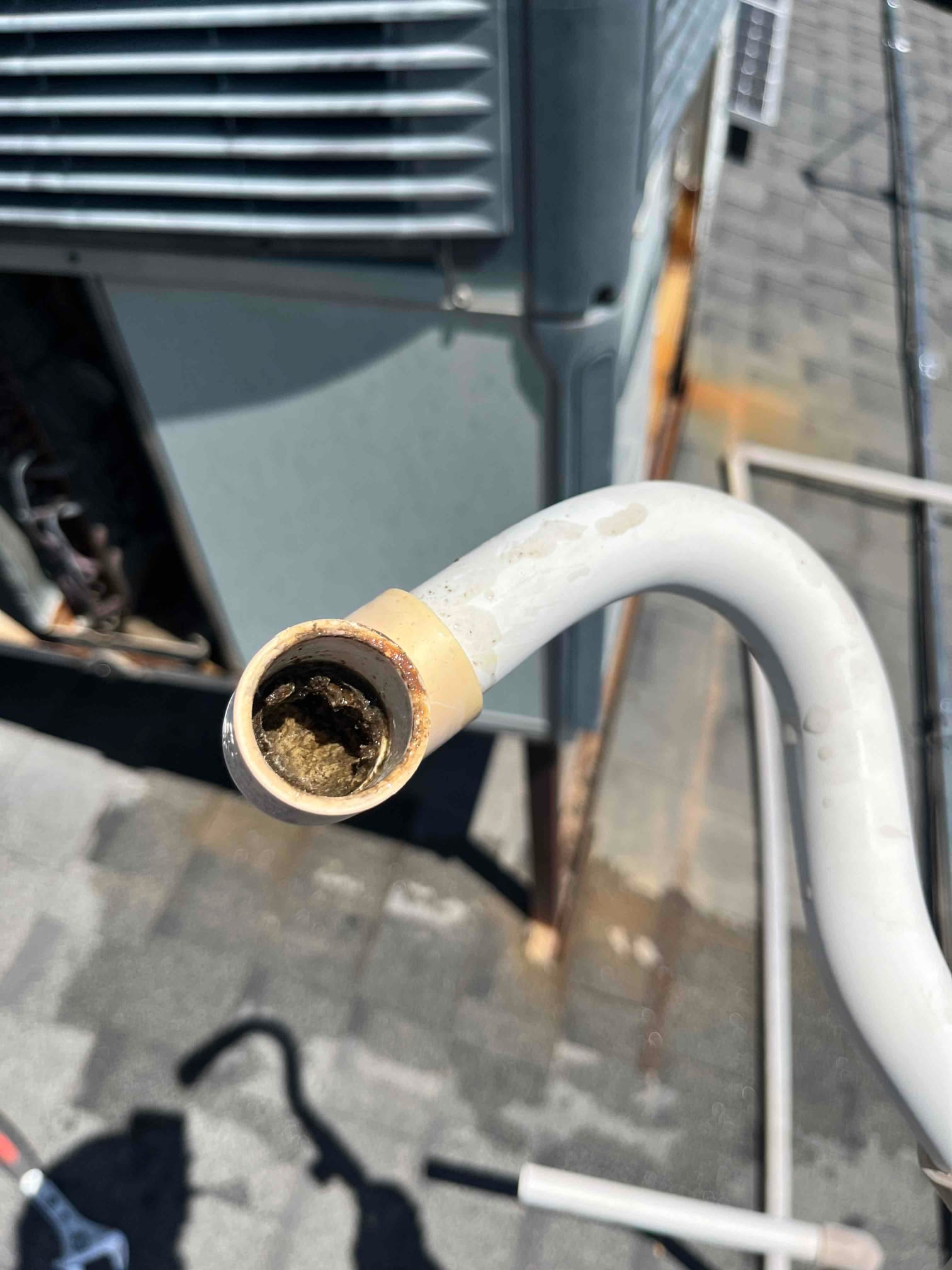 PVC condensate drain line end near rooftop condenser, with visible buildup inside the pipe opening.