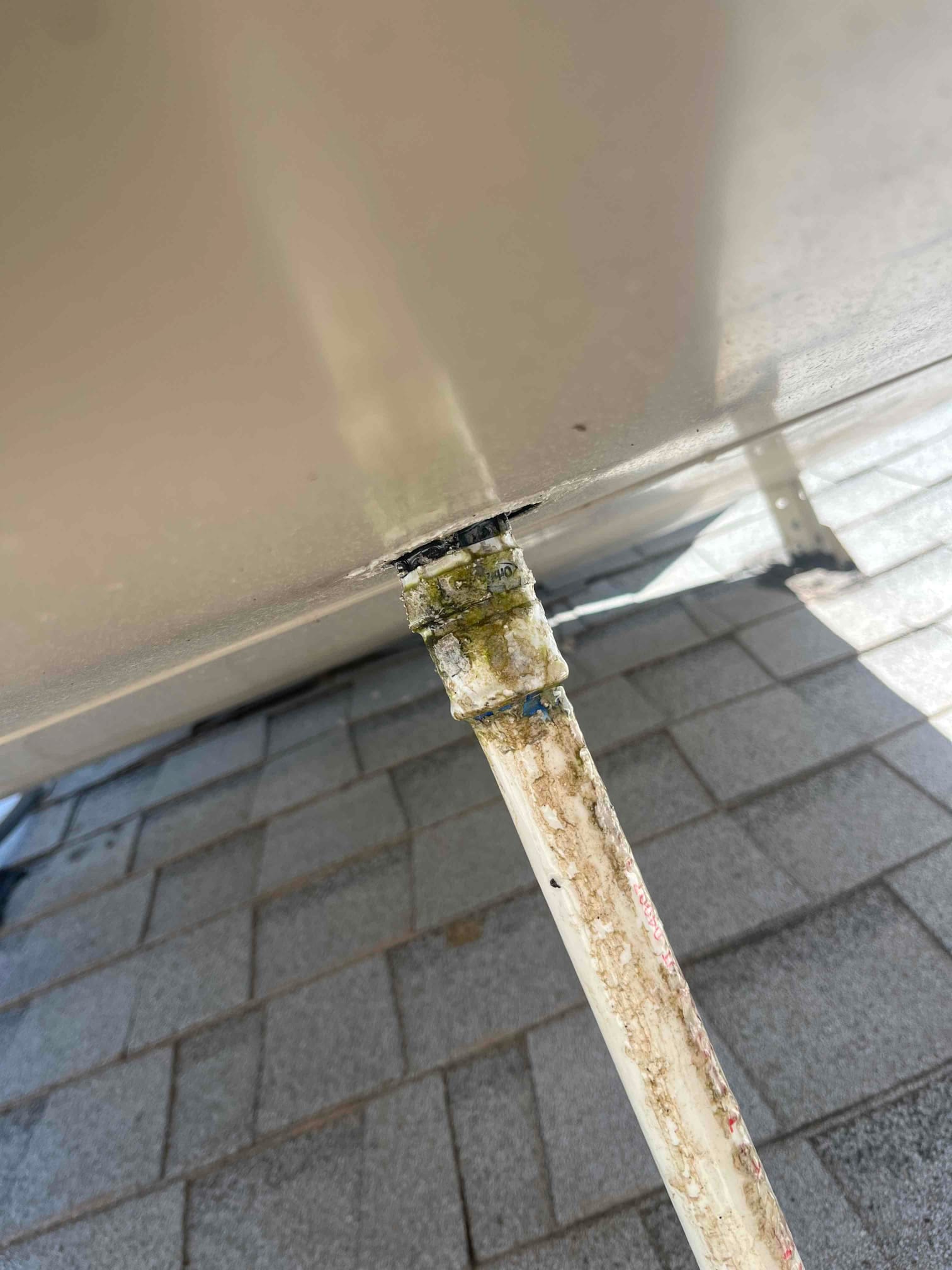 PVC condensate drain line exiting the unit’s base with heavy staining and green buildup around the joint.