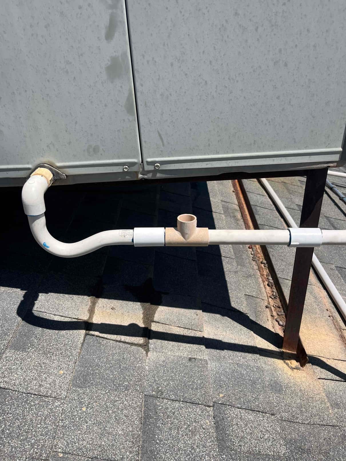 PVC condensate drain piping from rooftop HVAC unit with cleanout tee and unions over shingle roof.