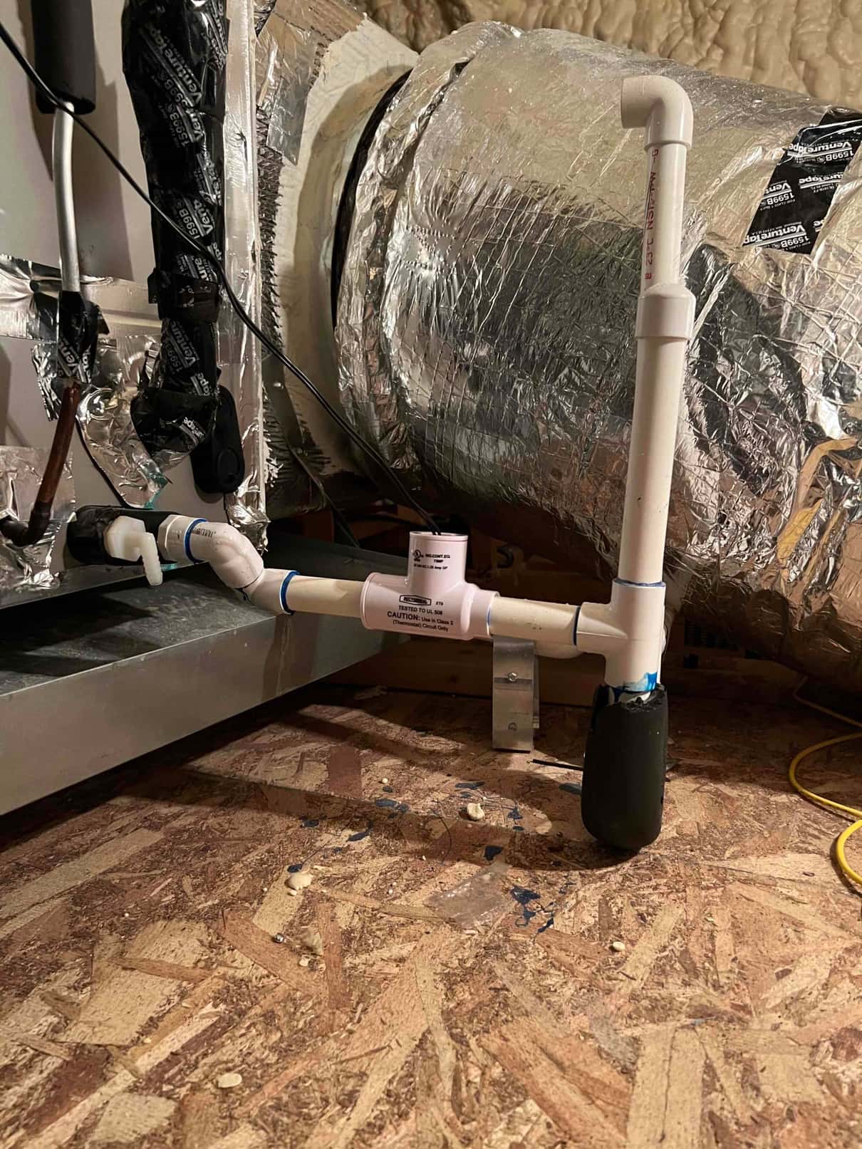 PVC condensate drain piping with tee, vertical vent riser, and insulated section installed beside the air handler.