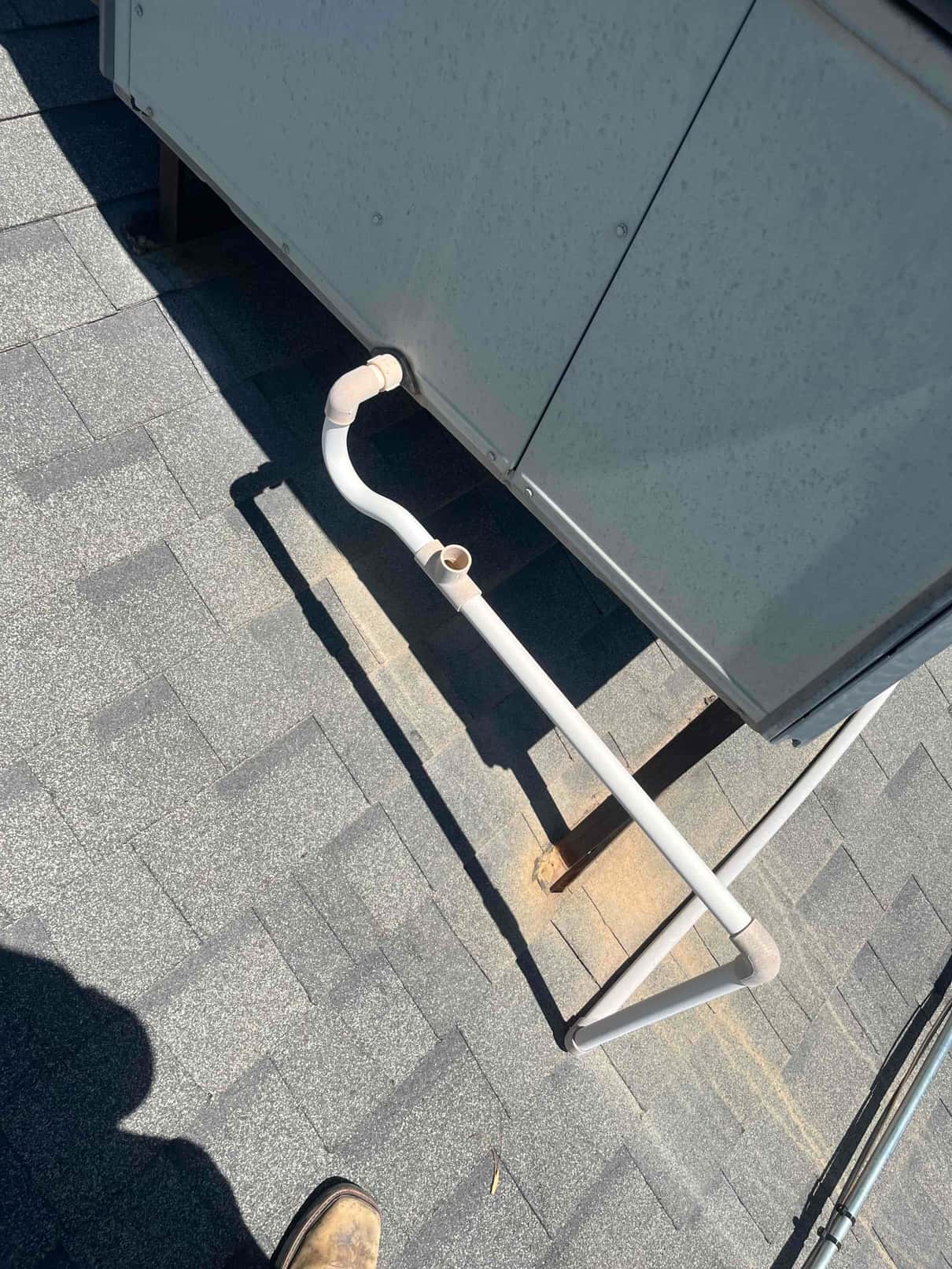 PVC condensate drain with trap and cleanout exits a rooftop HVAC unit and runs across shingles.