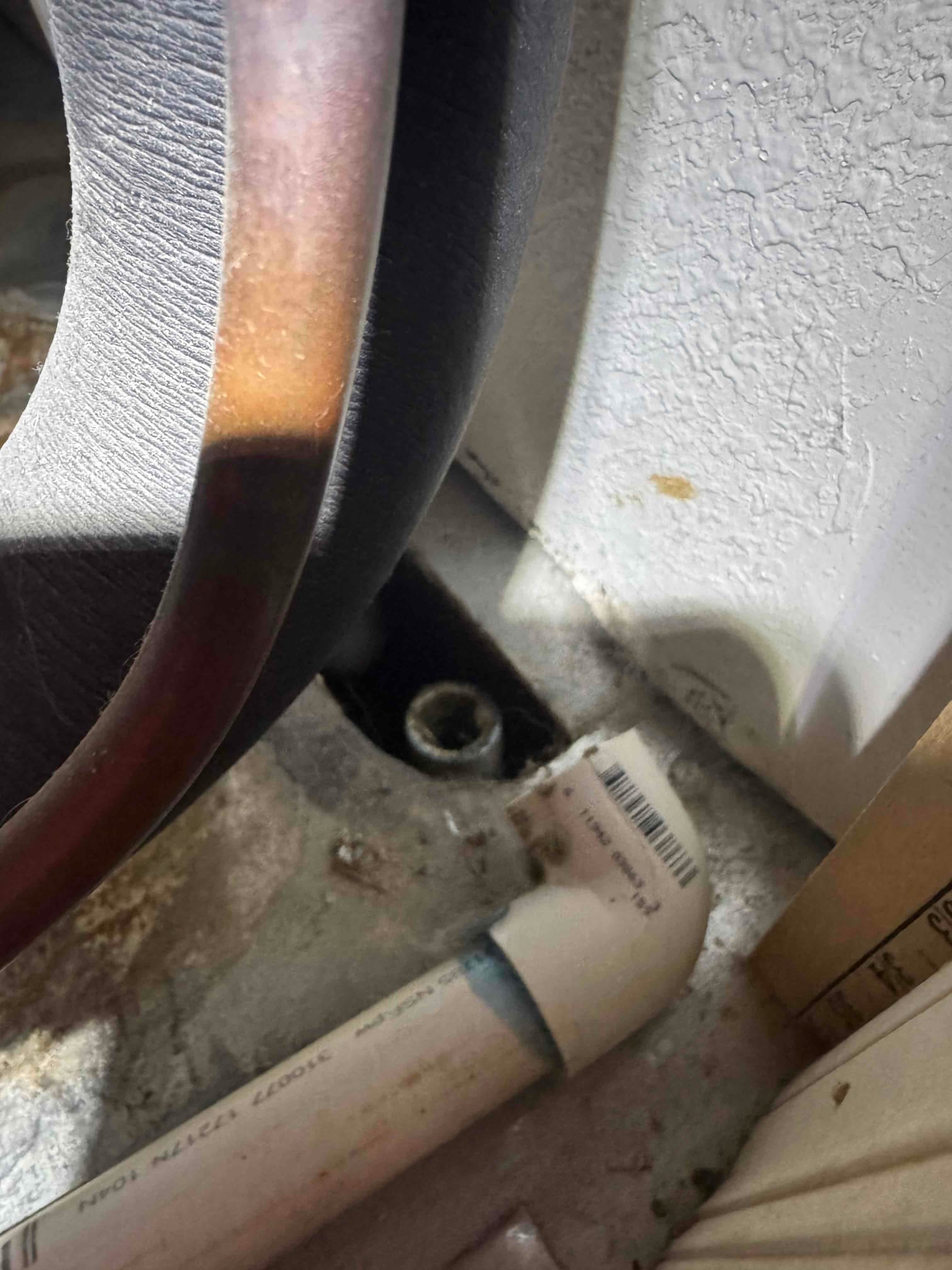PVC drain line with elbow at the air handler base, next to insulated copper line and mounting screw.