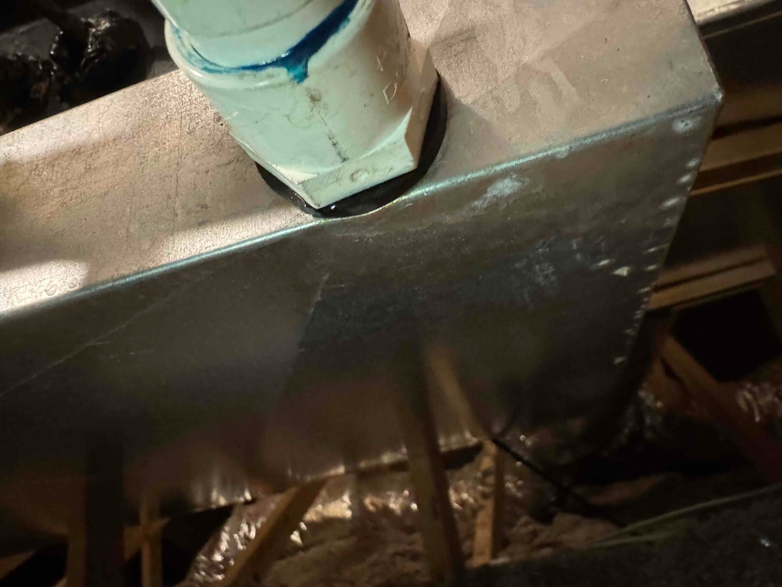 PVC pipe penetration sealed at a galvanized sheet-metal HVAC housing panel in the attic.