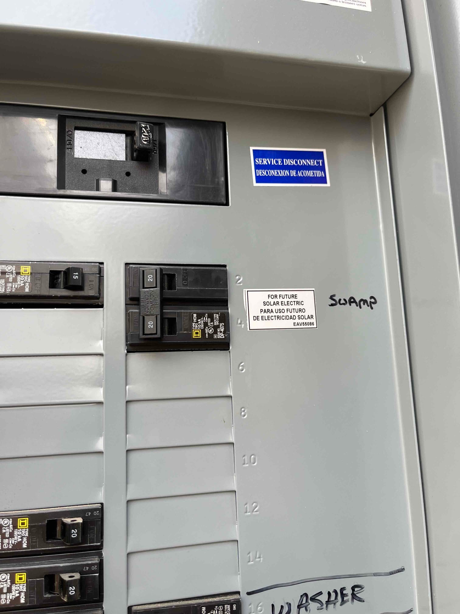 Residential electrical panel with multiple 20-amp breakers, labeled service disconnect sticker, and handwritten circuit labels including SWAMP and WASHER.