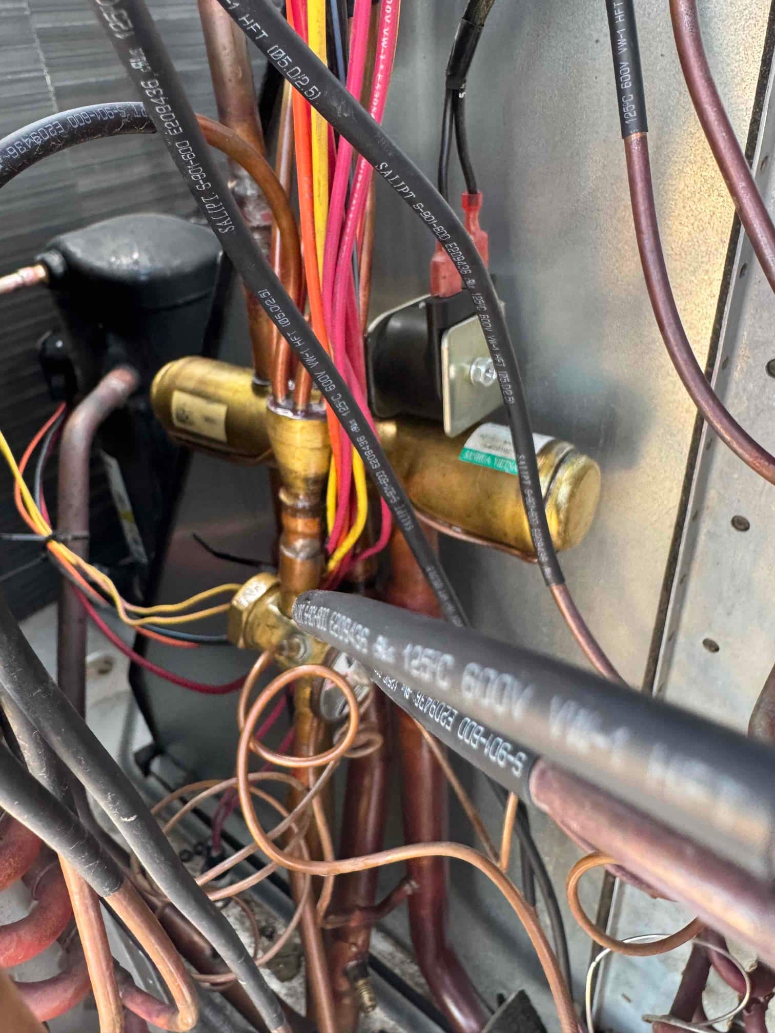Reversing valve and connected copper refrigerant lines inside the outdoor condensing unit, with wiring harness and compressor visible.