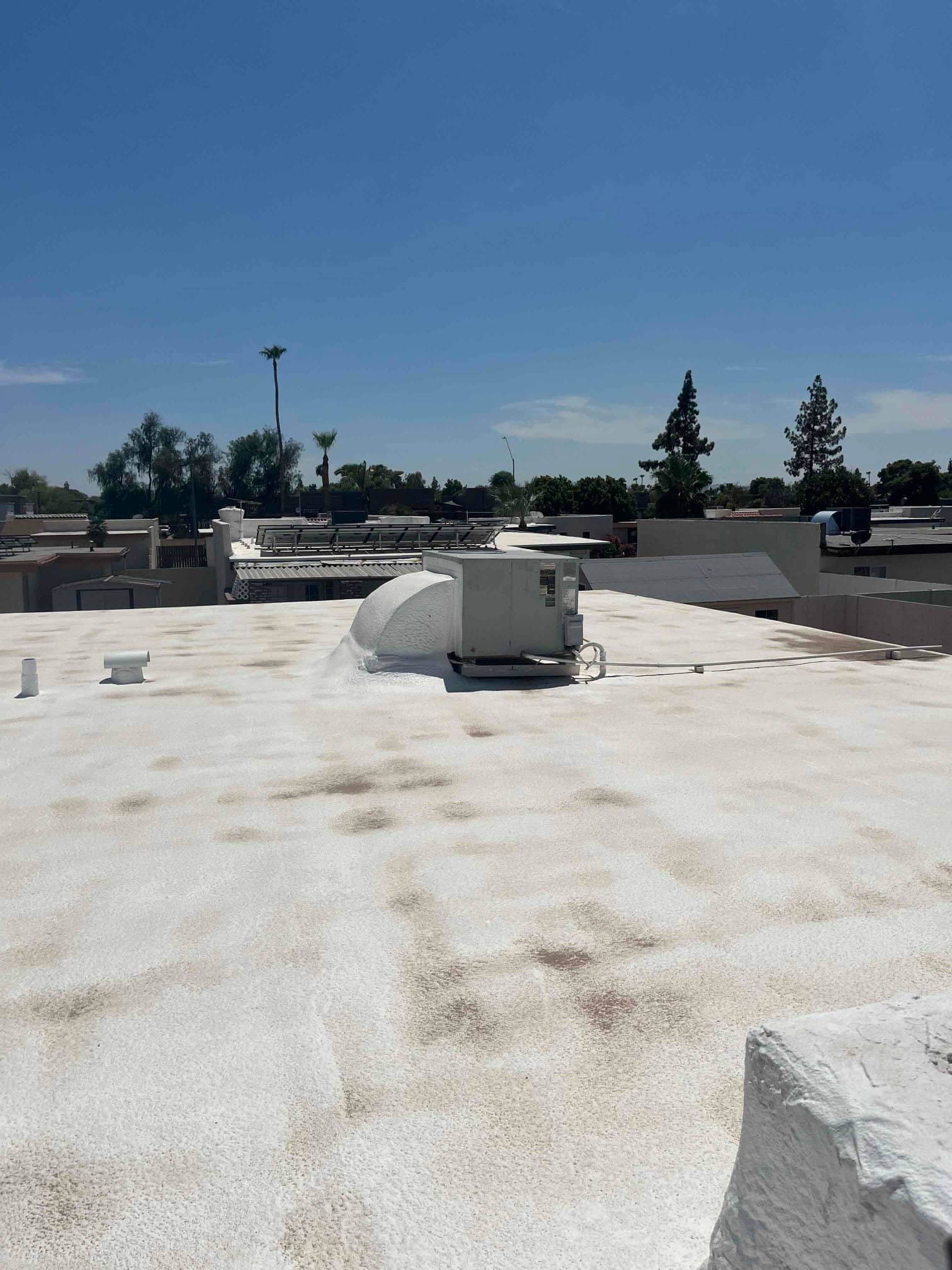 Roof-mounted HVAC unit on a flat white-coated roof, with flexible conduit and curb-mounted duct connection visible.