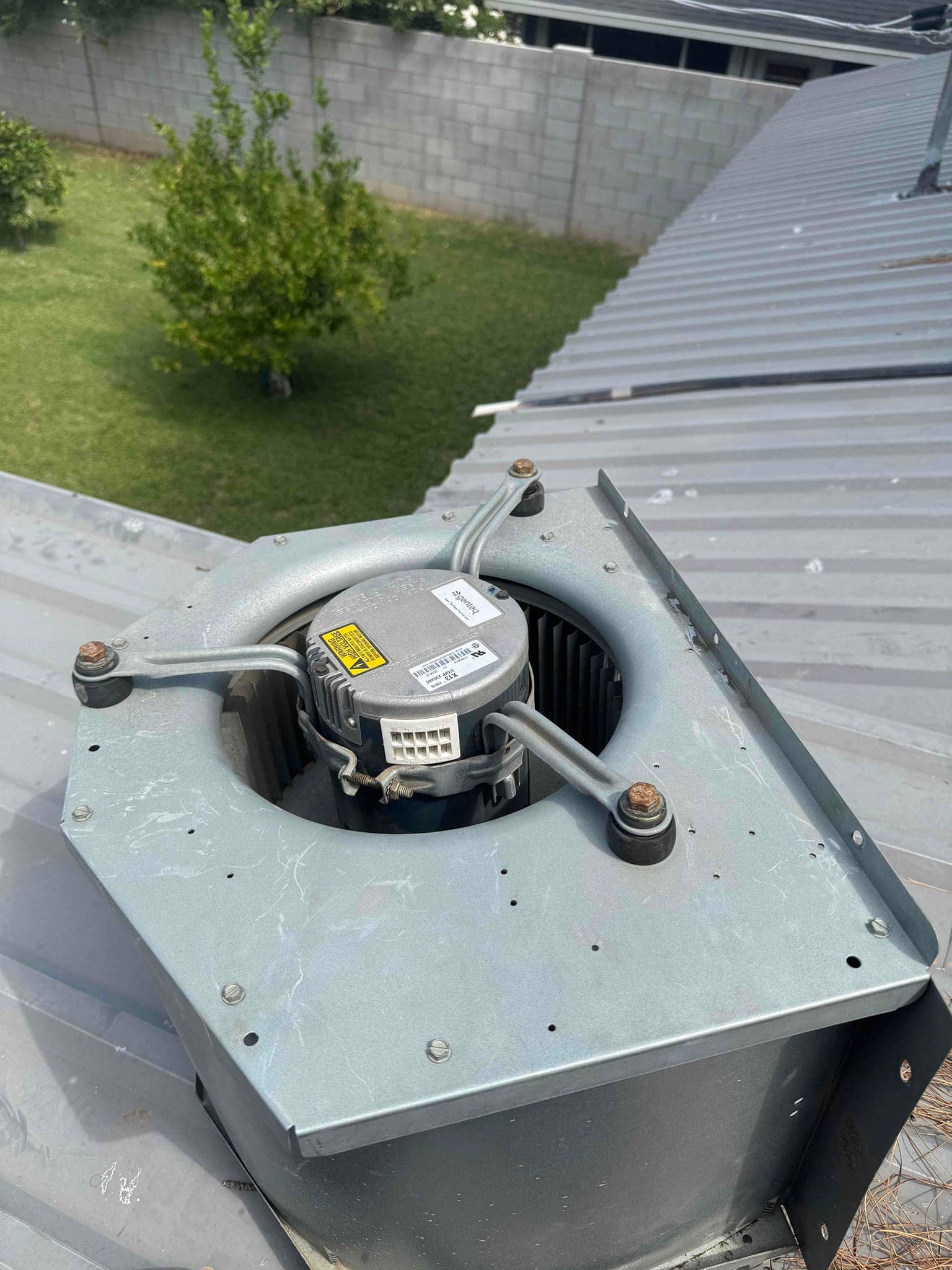 Rooftop blower assembly with motor and squirrel-cage wheel exposed on metal housing, with mounting bolts, support arms, and wiring connector visible.