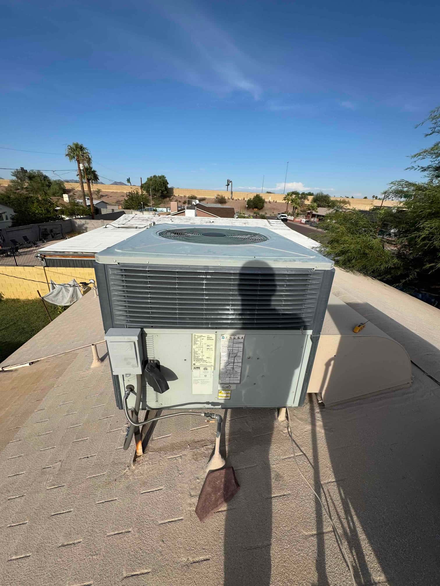 Rooftop HVAC condenser unit on mounting legs with service disconnect and flexible conduit visible at the side panel.