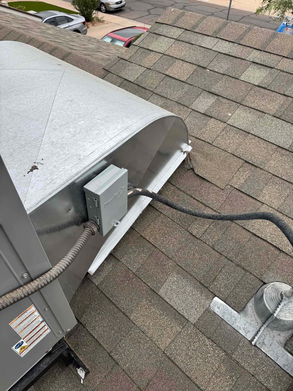 Rooftop HVAC package unit shown with weatherproof disconnect, flexible electrical conduit, and metal duct curb flashing at the shingle roof.