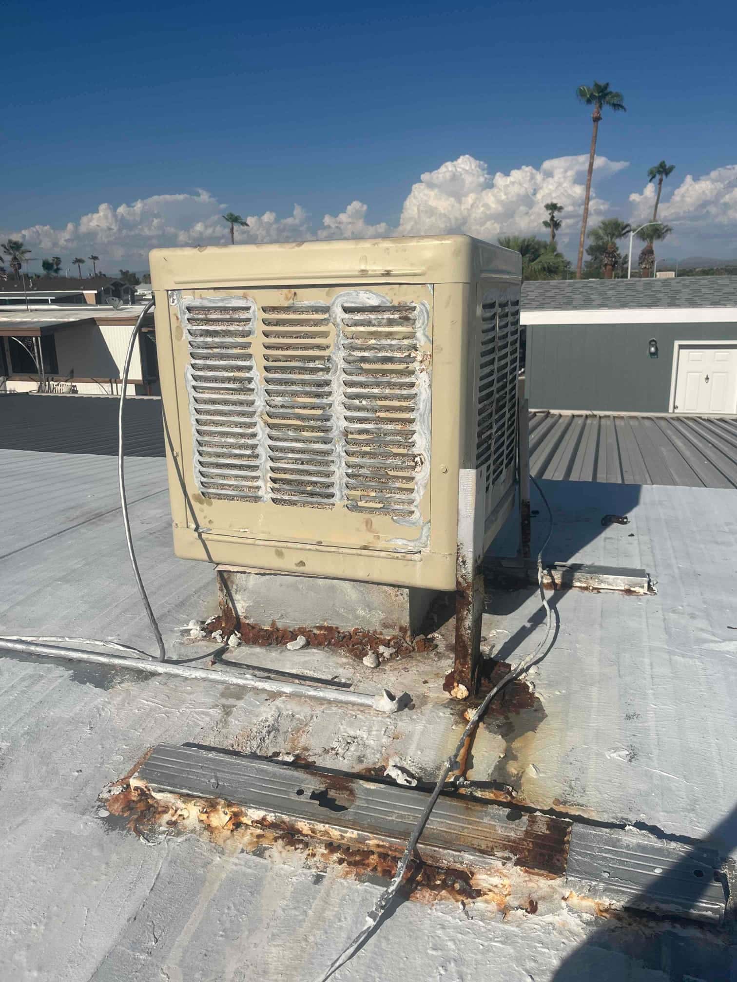 Rooftop HVAC unit with louvered panels shows rust on mounting rails and base, with sealant around curb and exposed wiring.