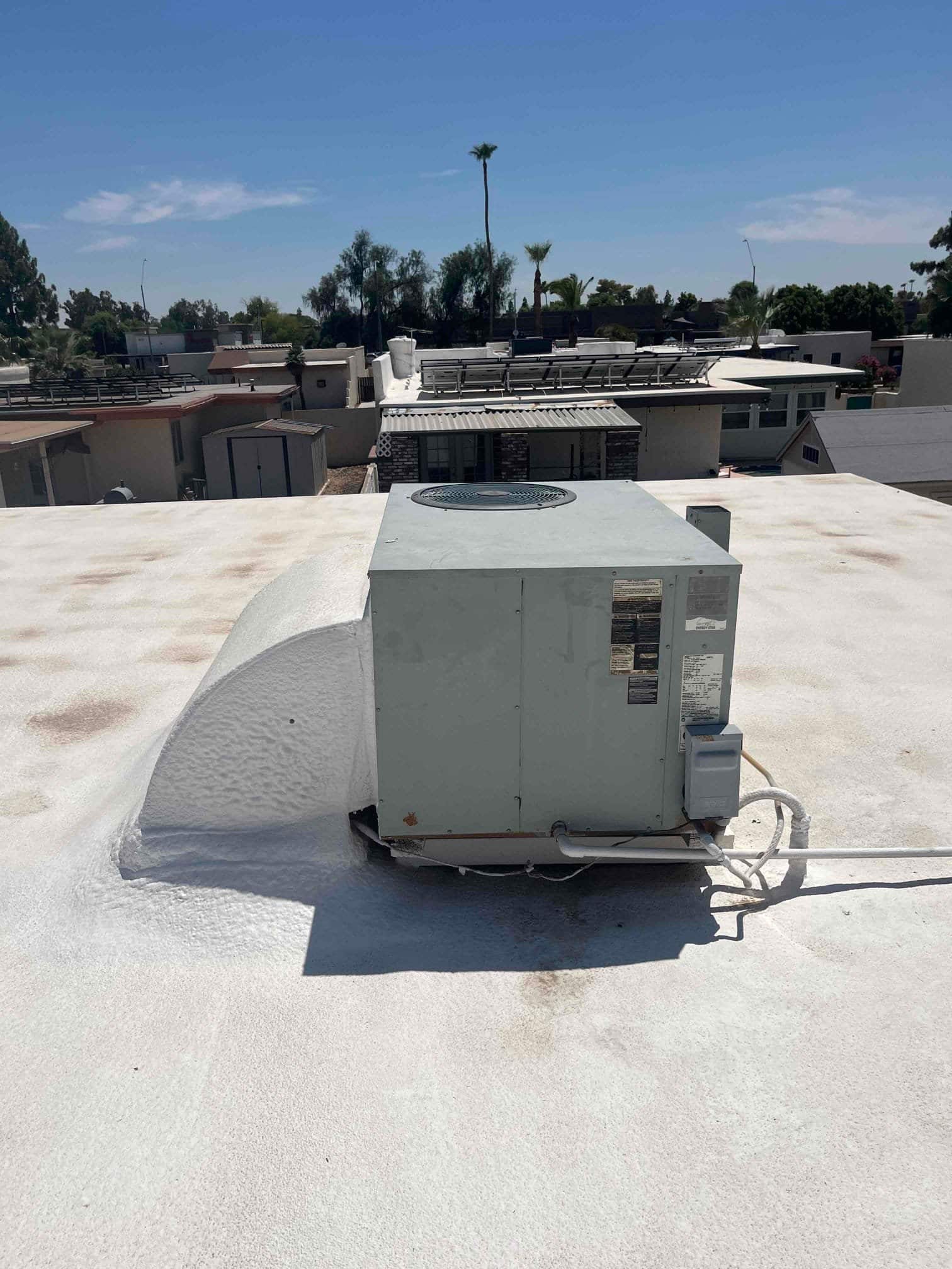 Rooftop package HVAC unit on a flat roof with disconnect box and condensate drain piping visible.