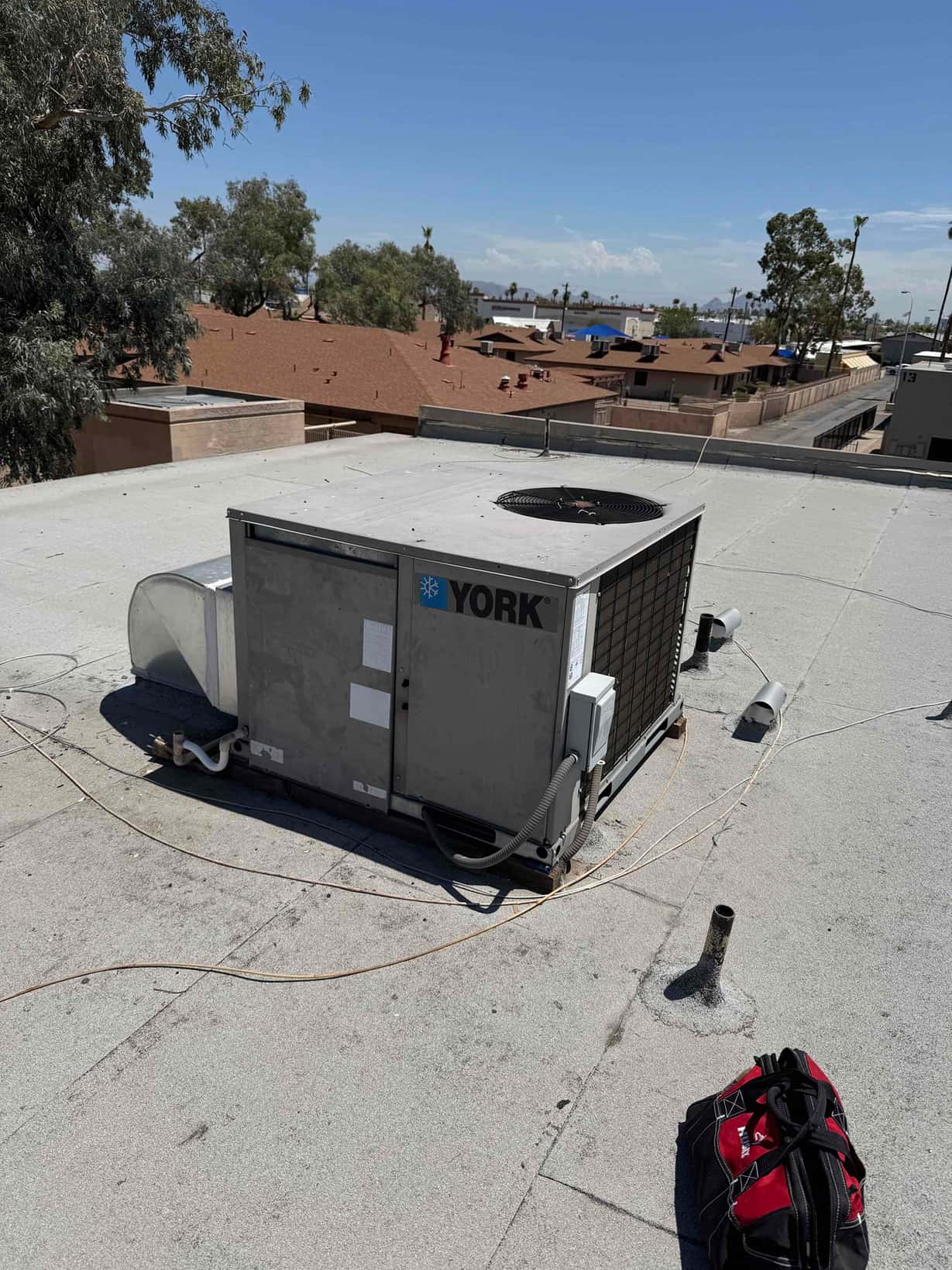 Rooftop package HVAC unit on a flat roof, with electrical disconnect, conduit, condensate drain, and service panels visible.