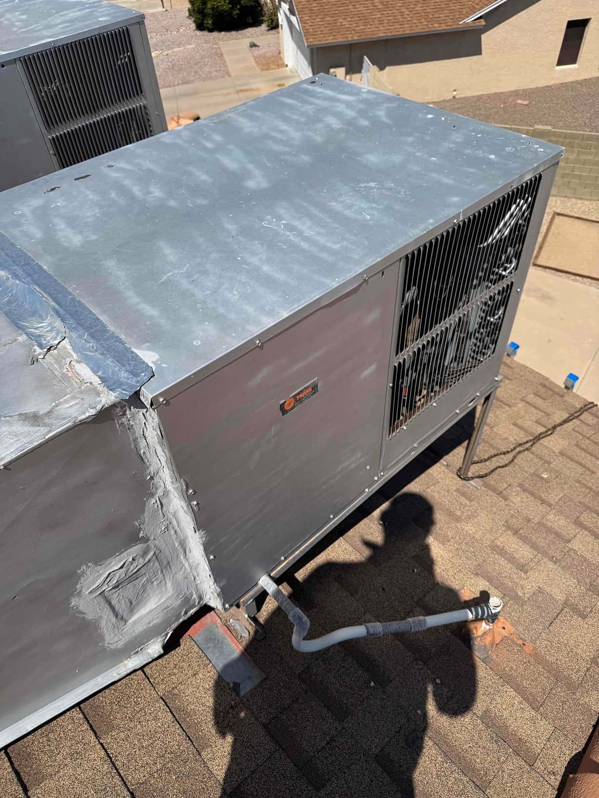 Rooftop package HVAC unit with mastic-sealed duct connection and PVC condensate drain on shingle roof.