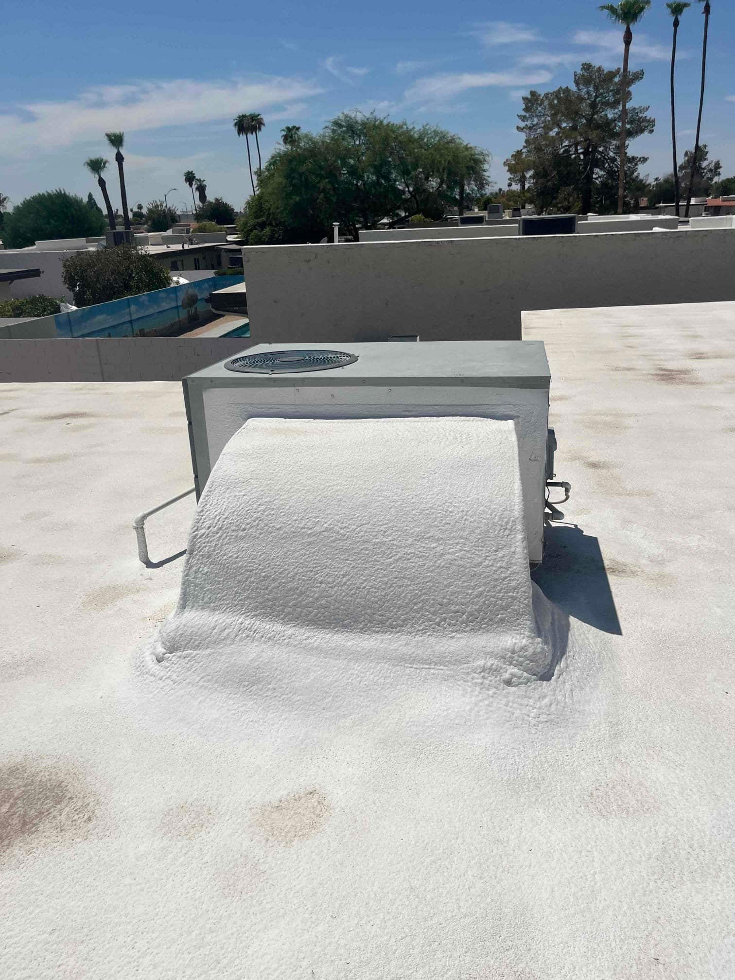 Rooftop package unit with condenser fan on a flat roof, curb and ductwork coated with roof sealant.