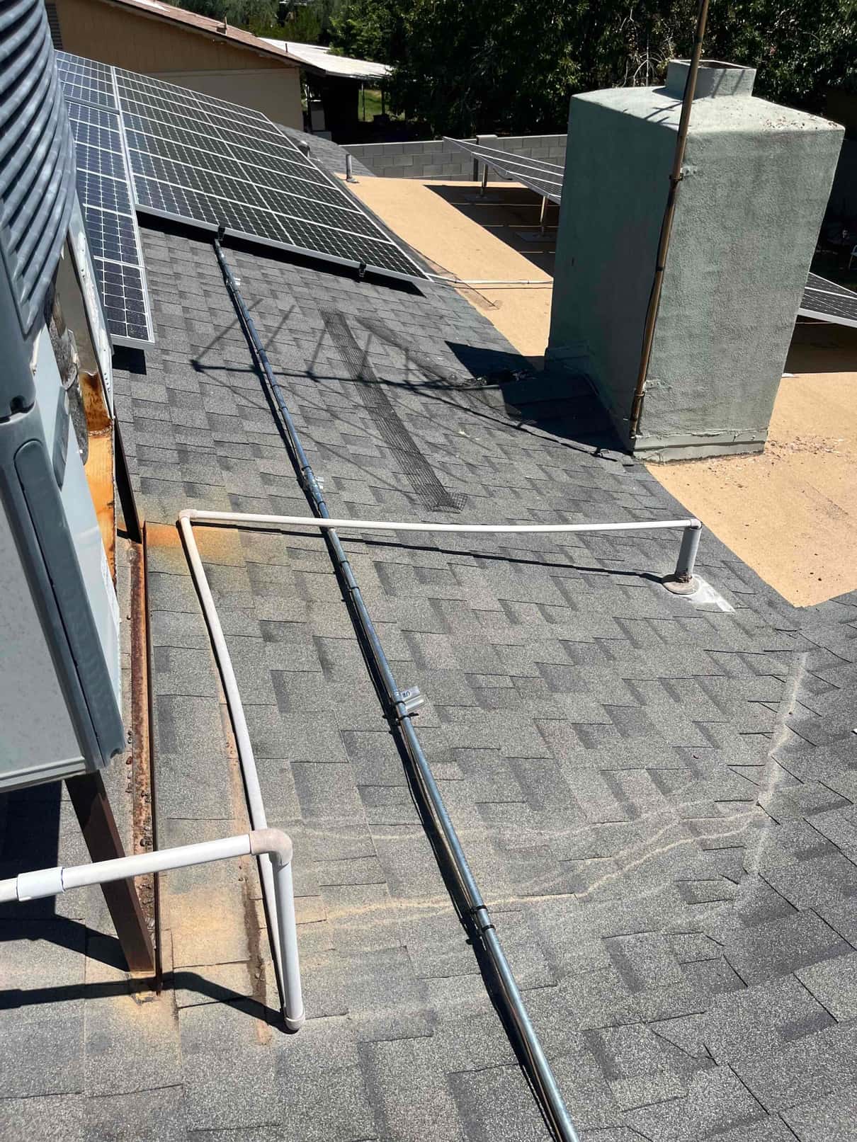 Rooftop package unit corner with PVC condensate drain and metal electrical conduit routed across shingles.
