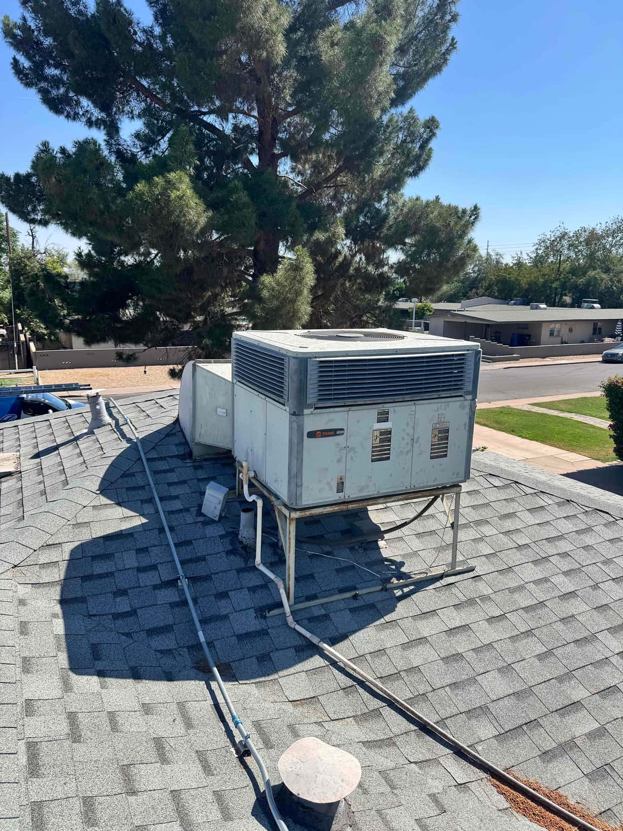 Rooftop packaged HVAC unit on curb with electrical conduit and refrigerant lines, showing surface rust on base supports.