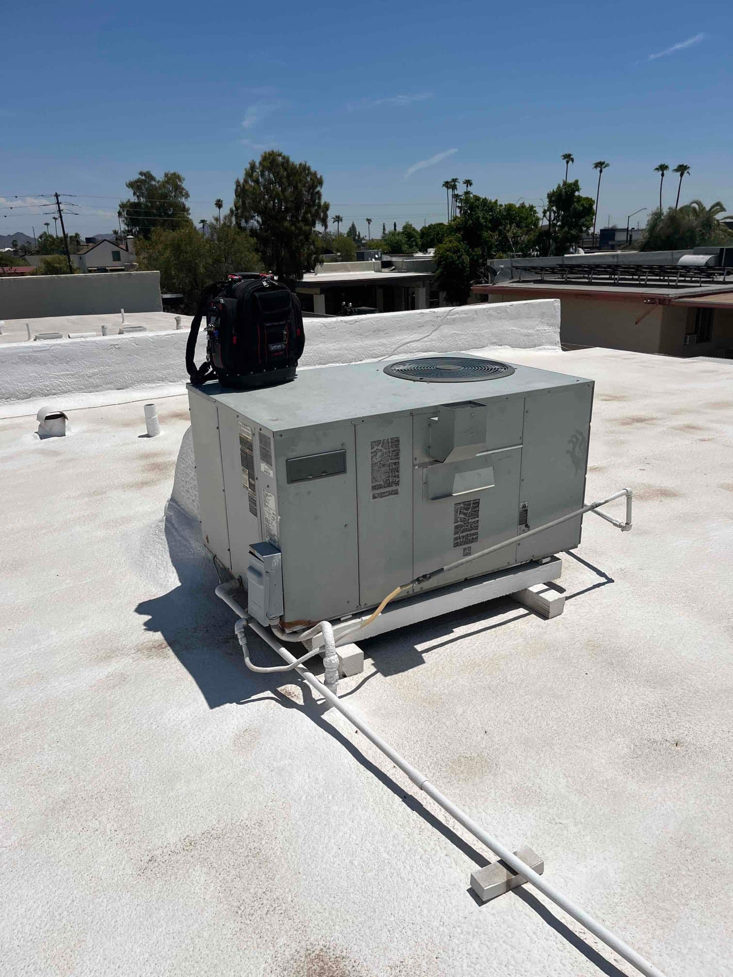 Rooftop packaged HVAC unit on a flat roof with connected electrical conduit and drain line.