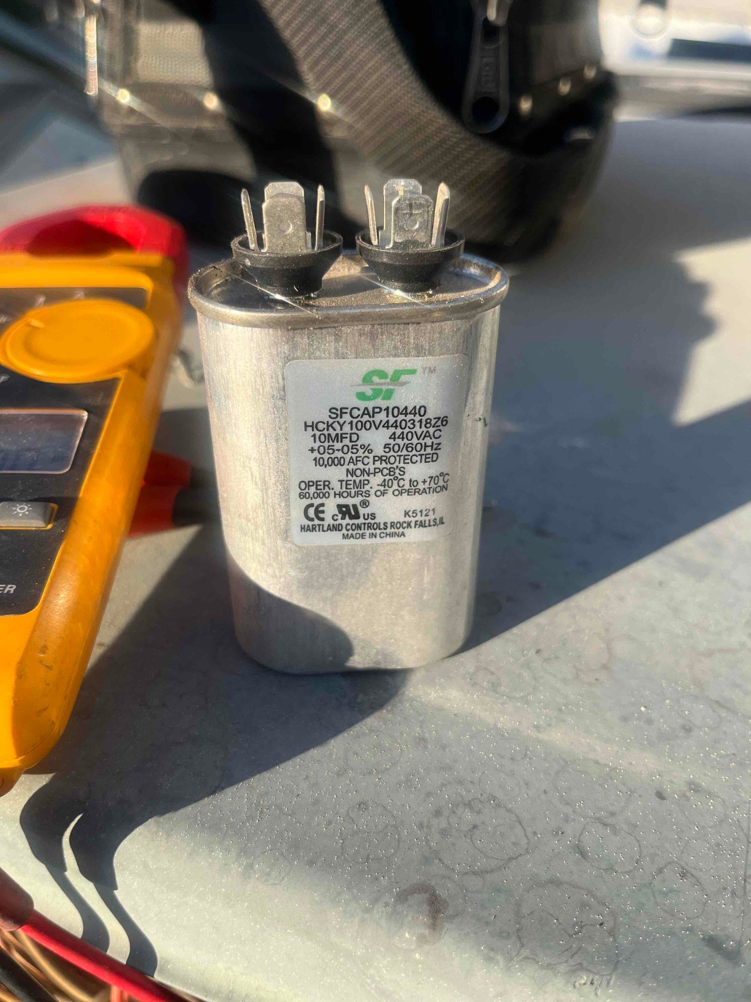 Round run capacitor labeled 10 MFD 440VAC with two spade terminals and rubber grommets, placed on a metal surface.