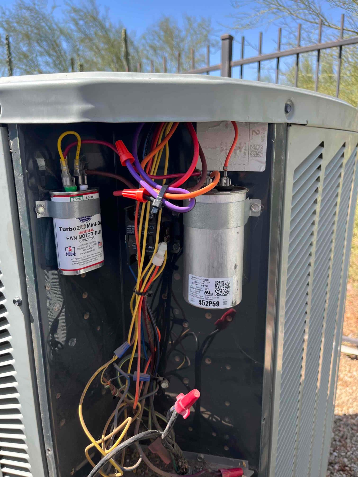Two run capacitors, a contactor, and connected wiring inside the outdoor condenser control compartment with the service panel removed.