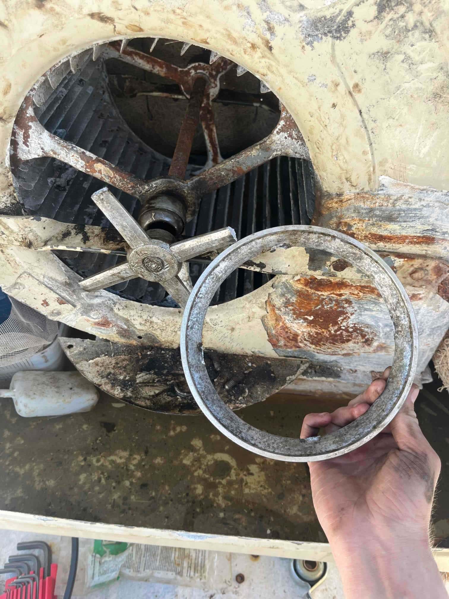 Rust-stained blower wheel and shaft inside housing; a hand holds a broken metal ring removed from the assembly.