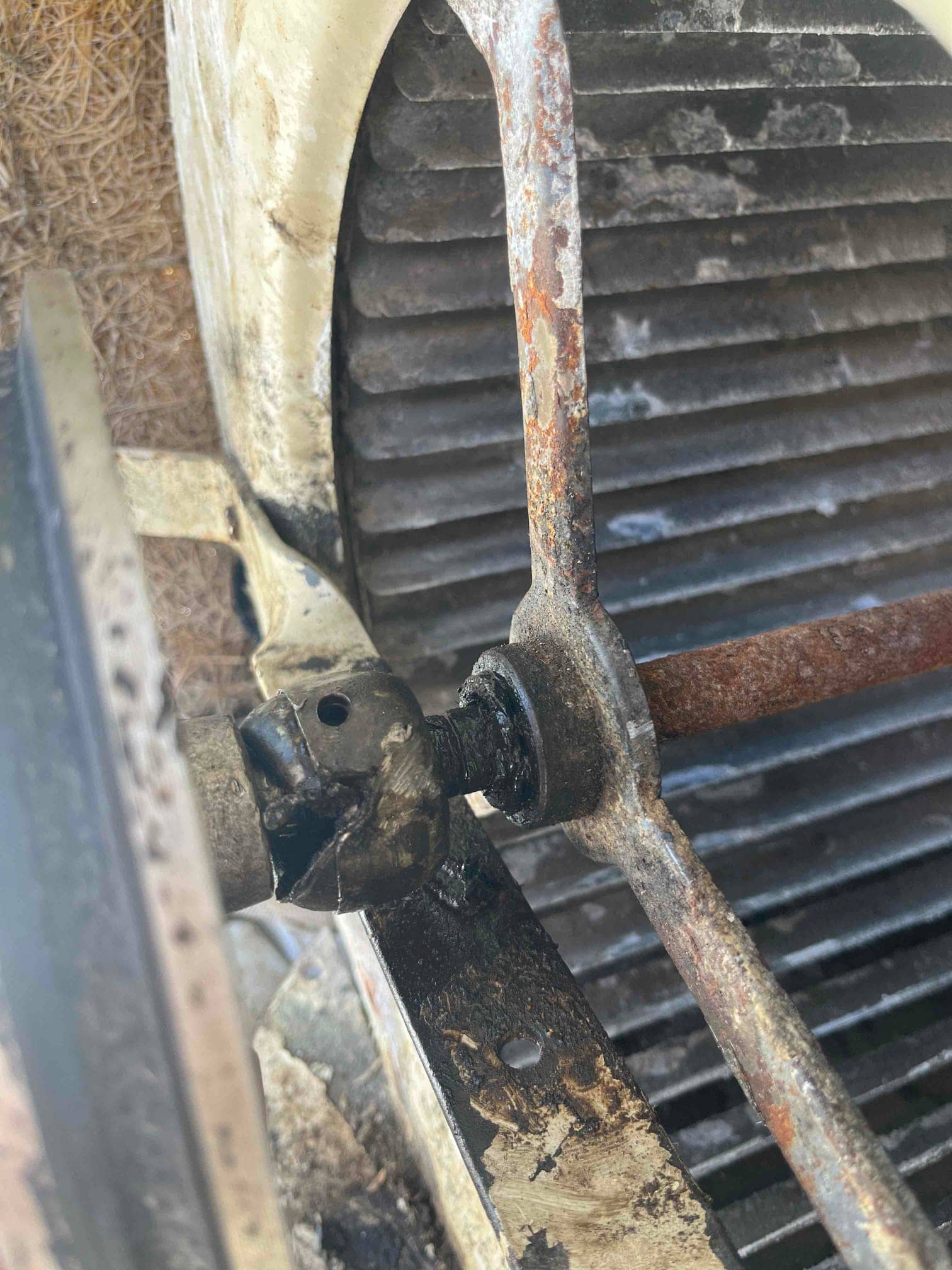 Rusted outdoor unit fan motor shaft and hub assembly, with set screw and weathered fan guard behind.