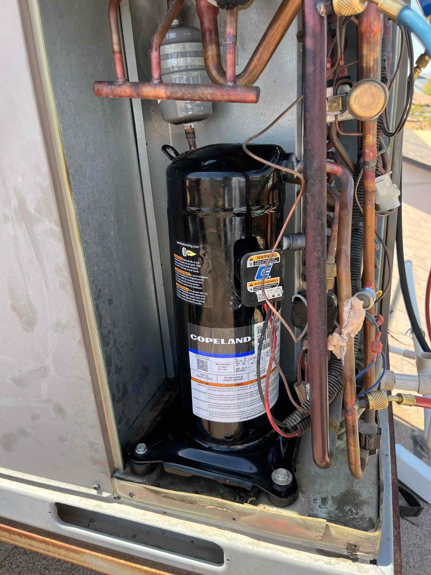 Scroll compressor mounted in condenser cabinet with connected copper refrigerant lines, accumulator, and service valve access fittings visible.