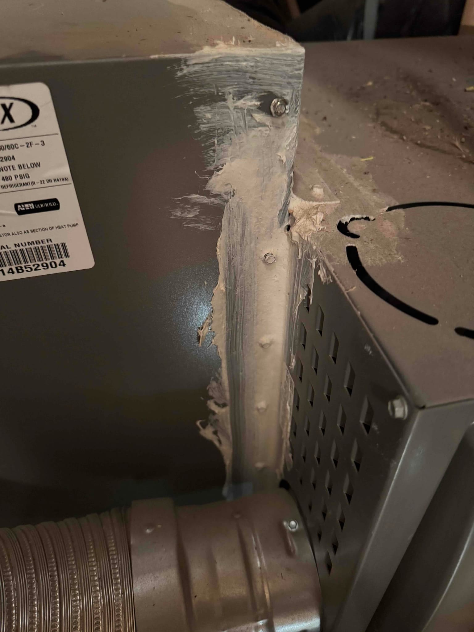 Sheet metal cabinet joint sealed with mastic and screws next to a round vent connector and louvered panel.