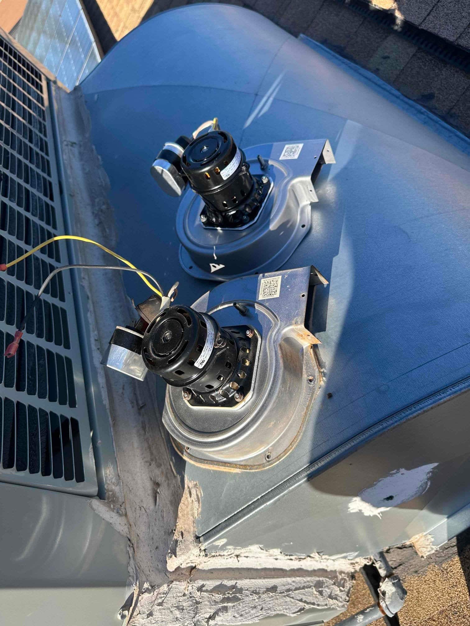 Two small motor-and-housing assemblies with attached capacitors on the rooftop HVAC unit cabinet.