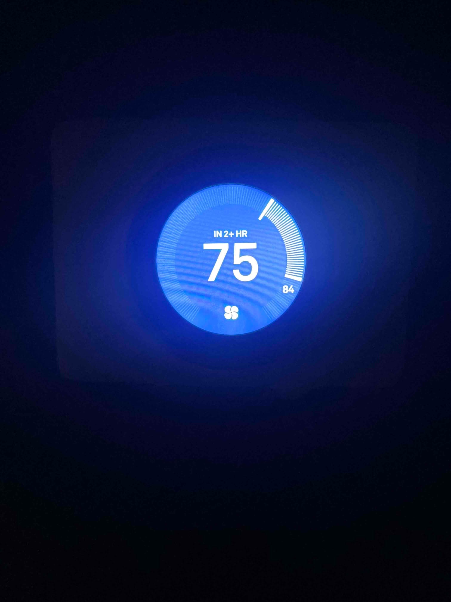 Smart thermostat display glows blue, showing 75 with 'IN 2+ HR' text, arc indicator, and fan icon.