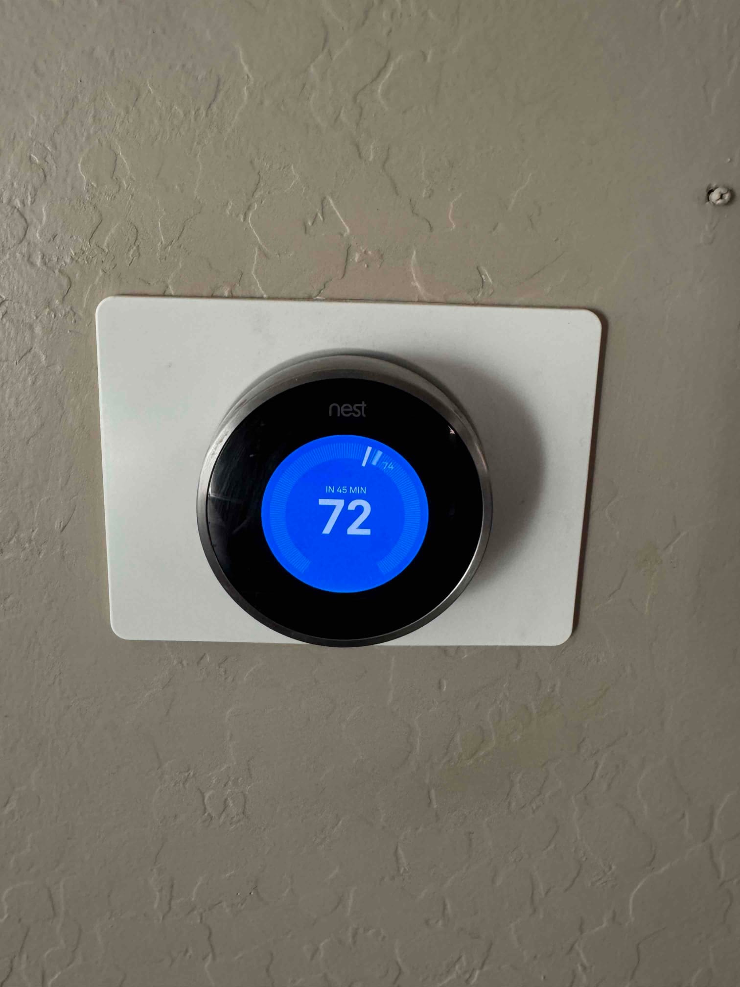 Smart thermostat displays cooling setpoint at 72 with estimated time remaining indicator on a wall plate.