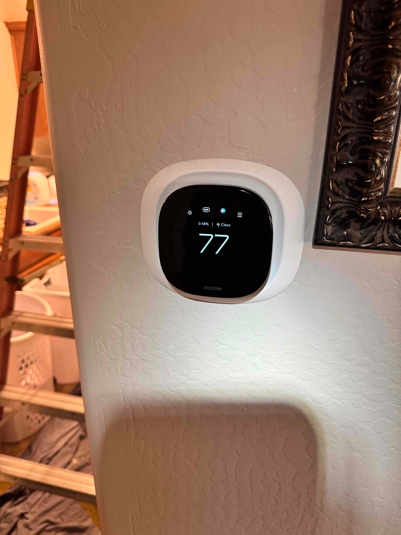 Smart thermostat on interior wall displaying 77 on the screen with icons above.