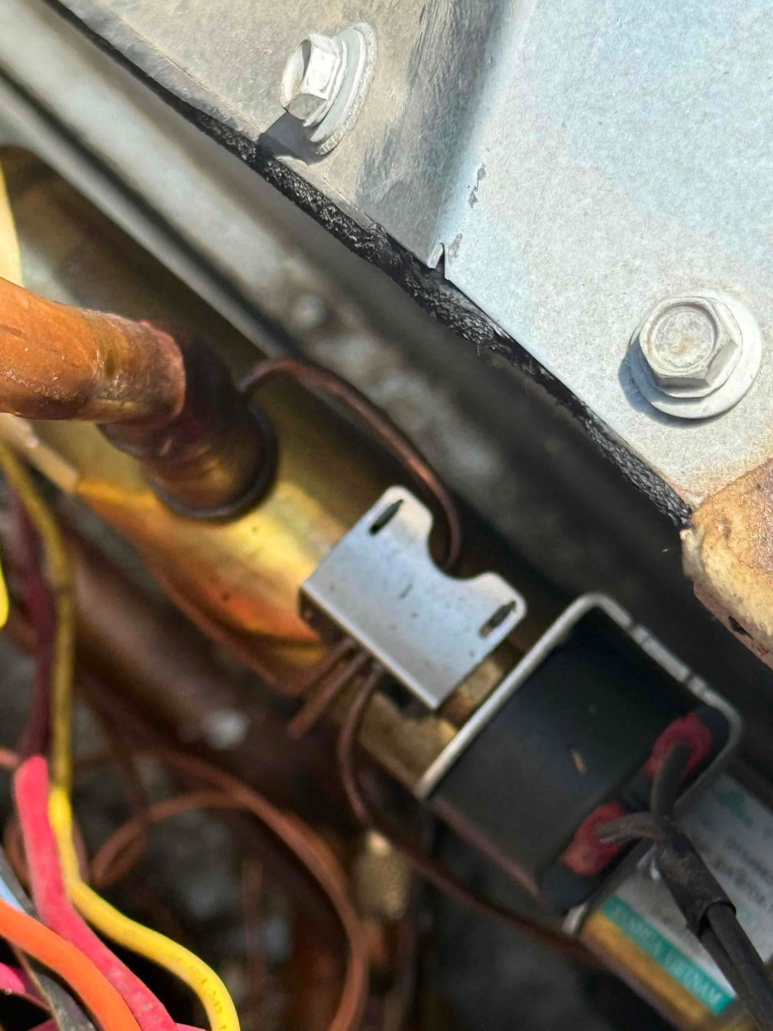 Solenoid valve assembly inside outdoor unit, showing brass valve body, black coil with retaining clip, and connected wiring.