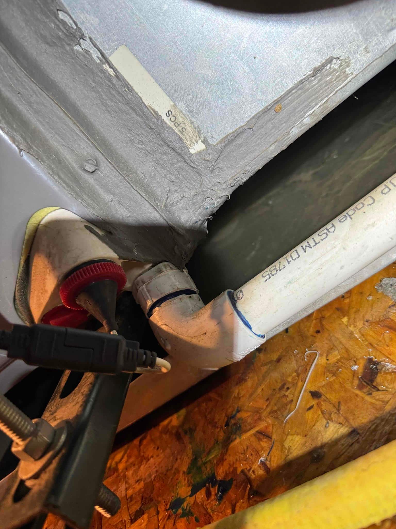 Standing water is visible in the drain pan beside the air handler’s PVC condensate drain and cleanout.
