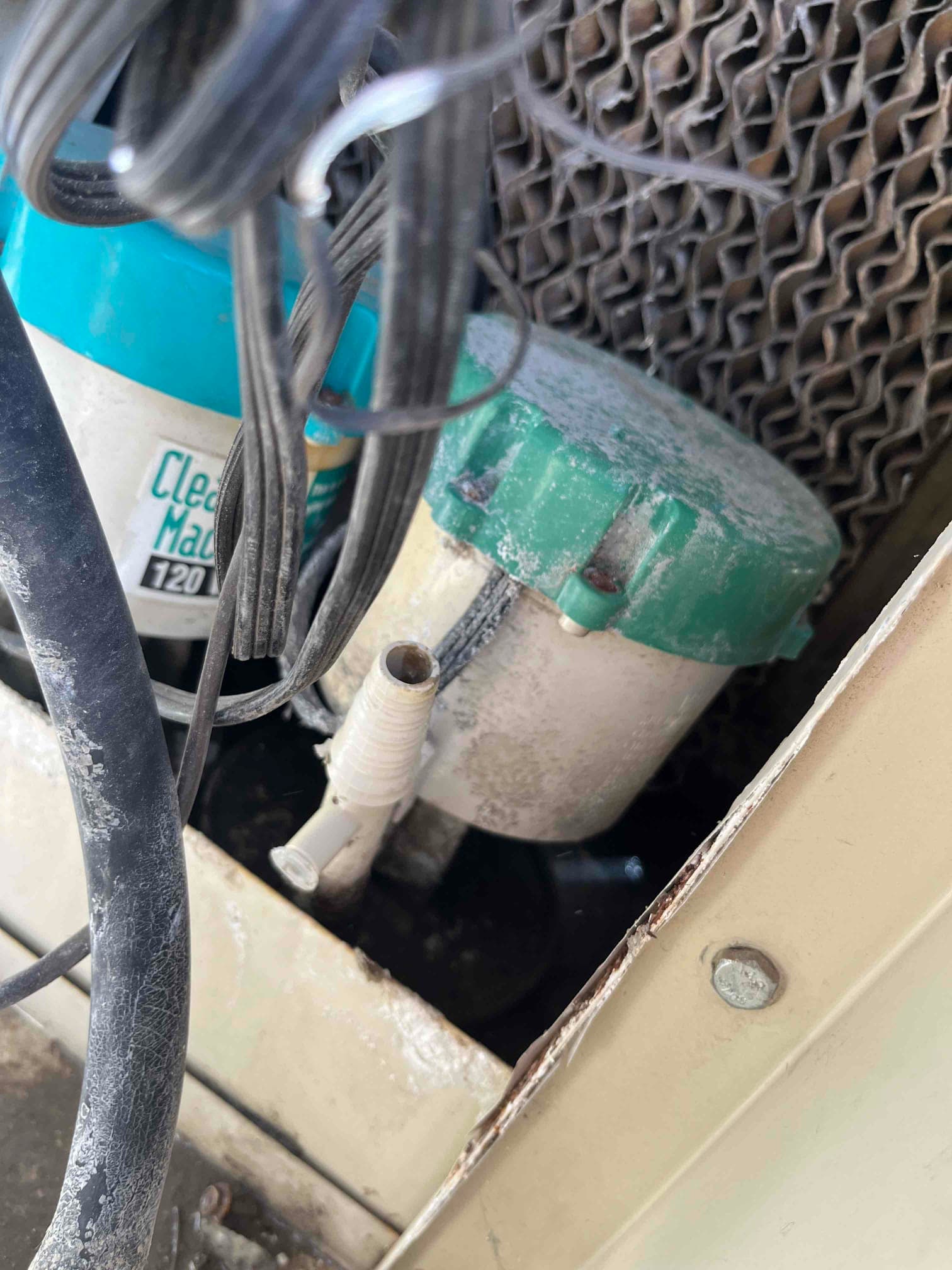 Submersible water pump with green cover and barbed outlet beneath honeycomb cooler pad, with bundled wiring routed nearby.