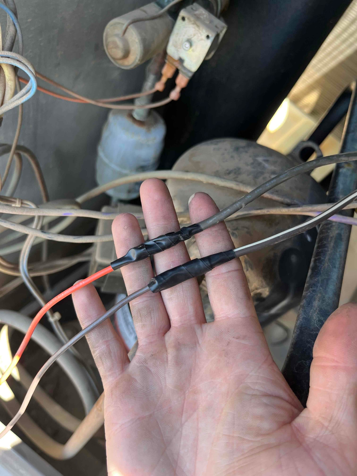 Technician hand holds three spliced wires wrapped with black electrical tape inside condenser near compressor and contactor.