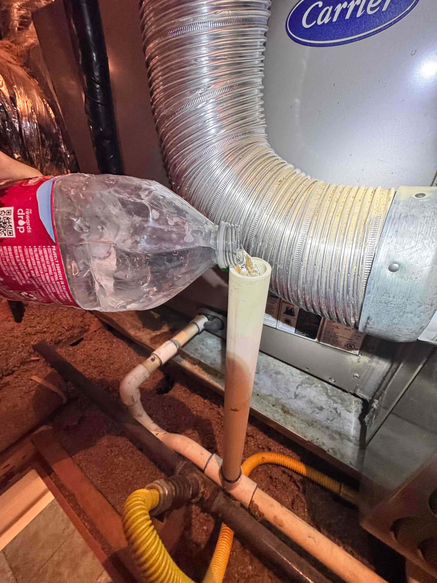 Technician pours liquid from a bottle into the condensate drain cleanout near the indoor unit and drain piping.