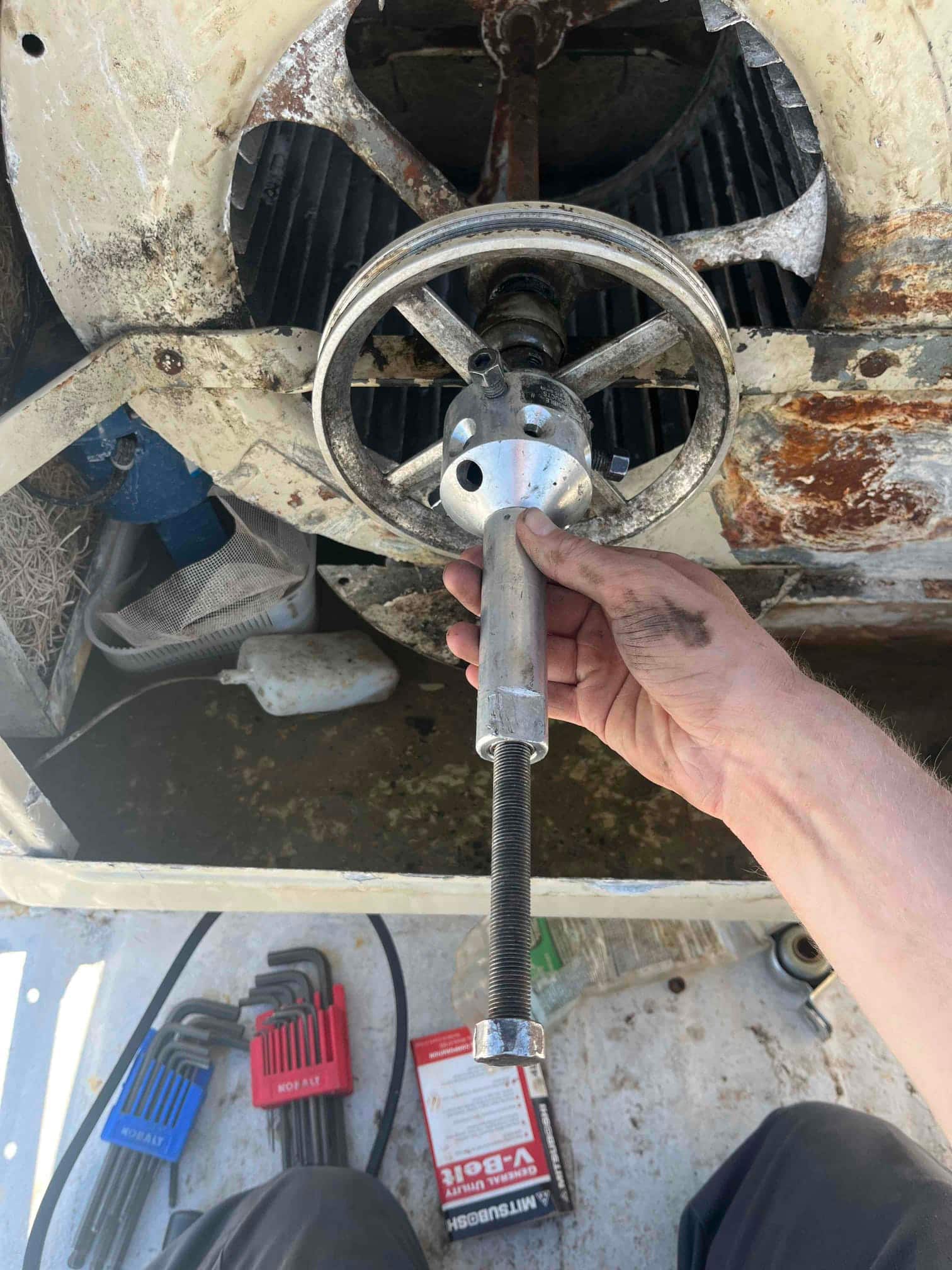 Technician uses a puller tool on a rusted blower pulley and shaft within the blower housing.